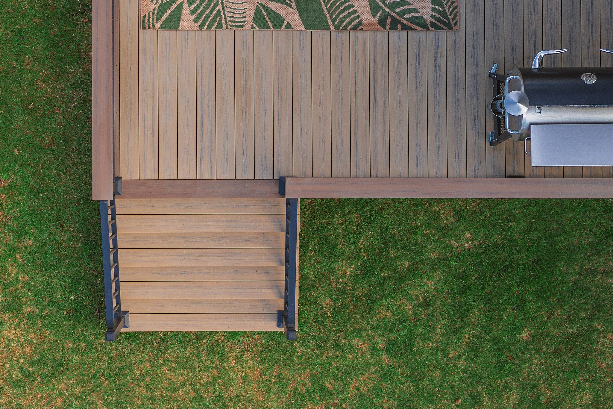Top-down view of a backyard deck with a barbecue grill, a rug, and a composite deck.
