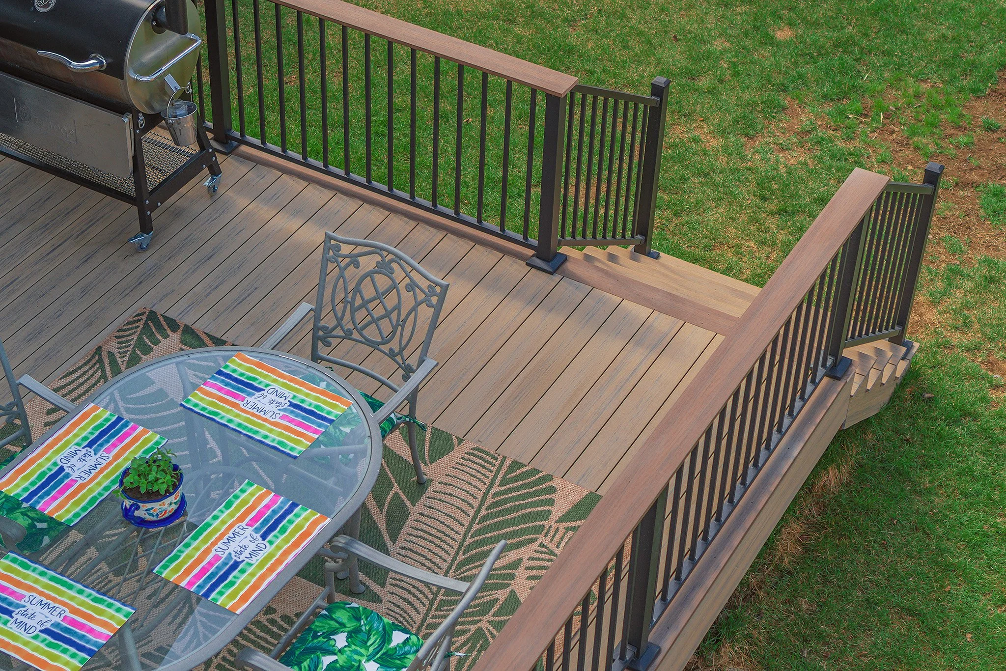 A composite deck with black metal railing, outdoor furniture, and a barbecue grill, overlooking a lawn.