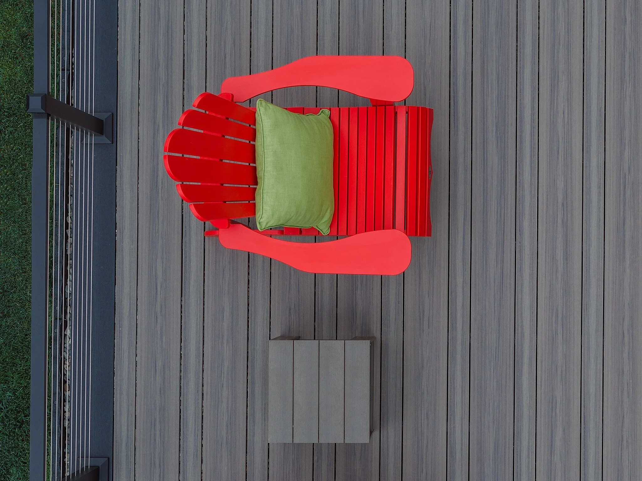 Red Adirondack chair with green cushion on a composite deck, with a metal aluminum railing and grassy area visible to the side.