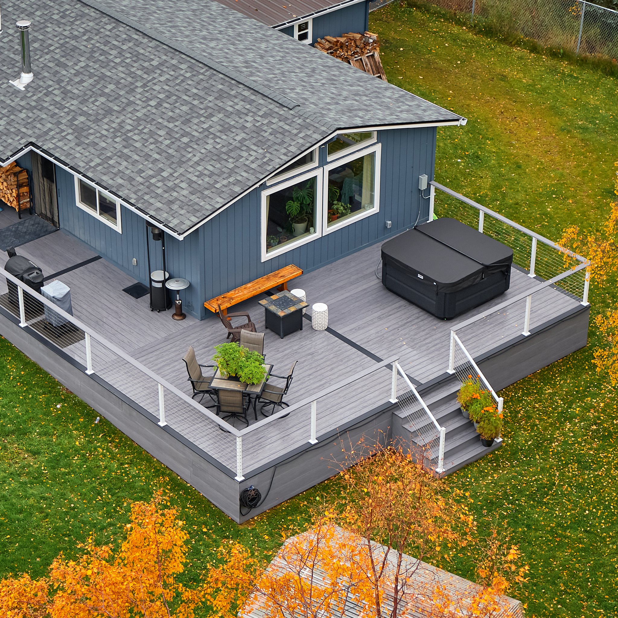 Aerial view of a house's backyard deck with outdoor furniture, a hot tub, and autumn trees.