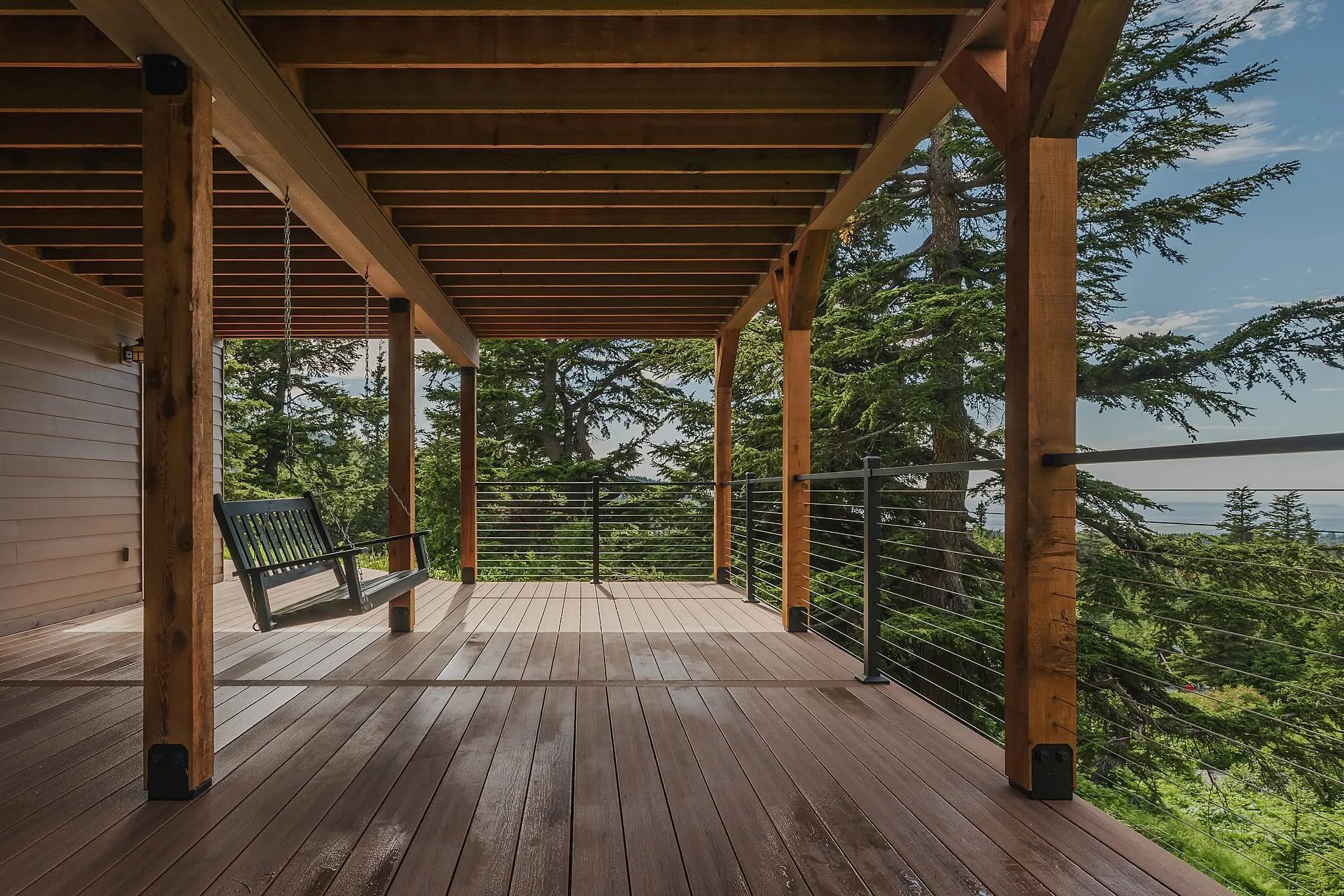 Composite decking balcony with a swing bench overlooking a lush green forest and cloudy sky in the distance.
