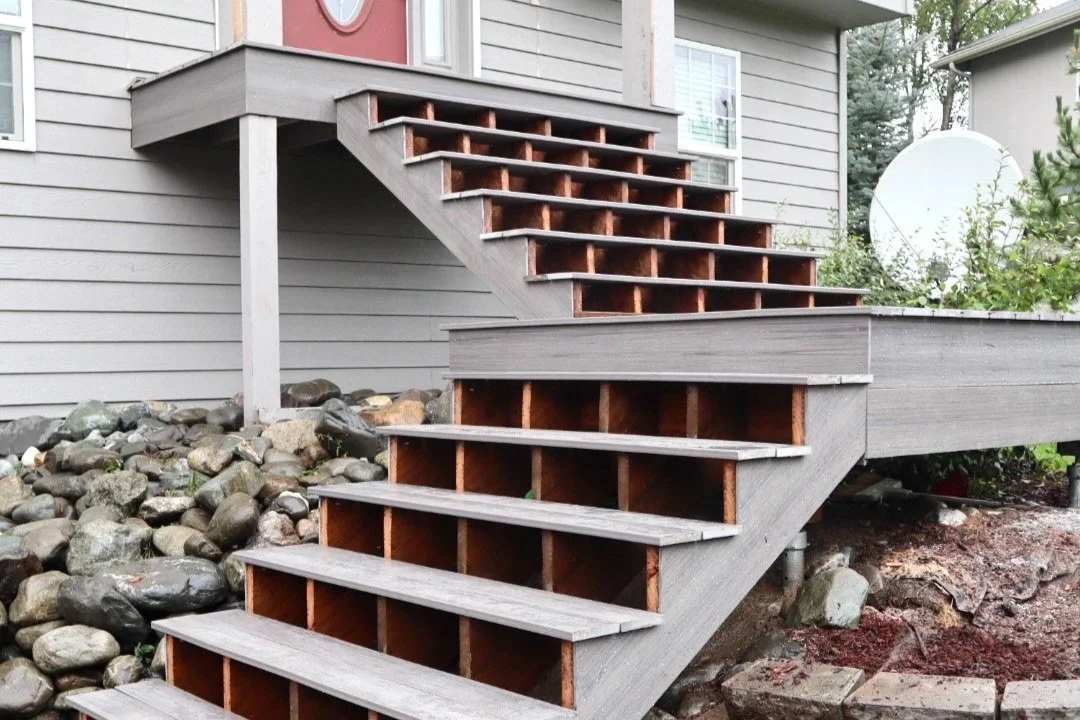 Image of a house exterior showing a composite staircase with open risers and a landing, leading from the ground to an elevated deck.