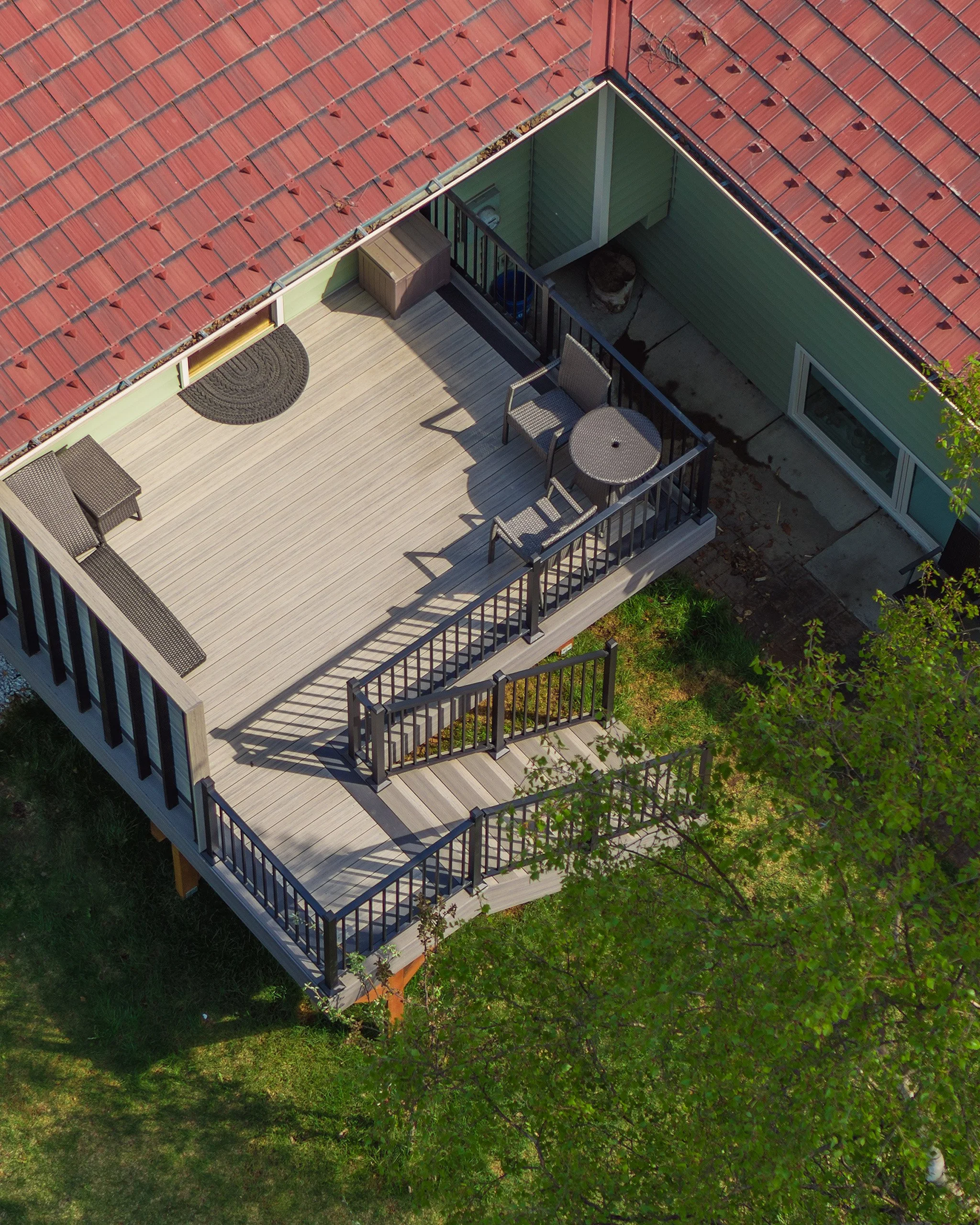 Aerial view of a house deck with outdoor furniture, railing, and a red shingled roof.