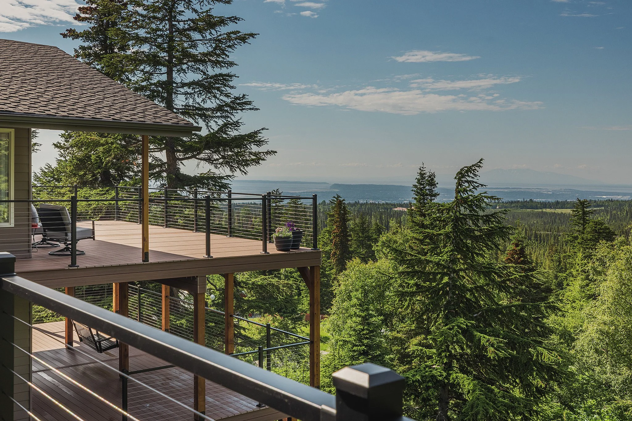 View of a composite deck on a house overlooking a forest and distant mountains under a blue sky with scattered clouds.