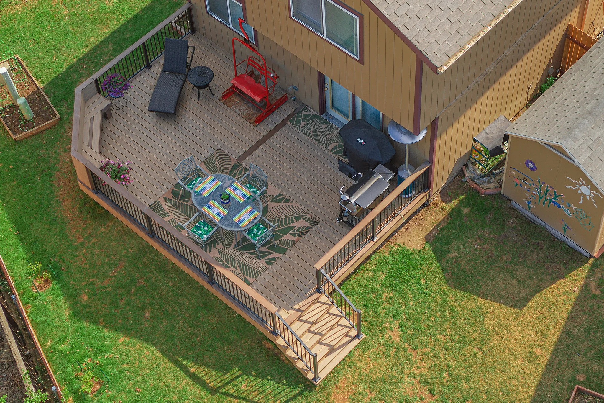 A house's backyard deck with outdoor furniture, a barbecue grill, a patio heater, and a garden area with a painted fence.