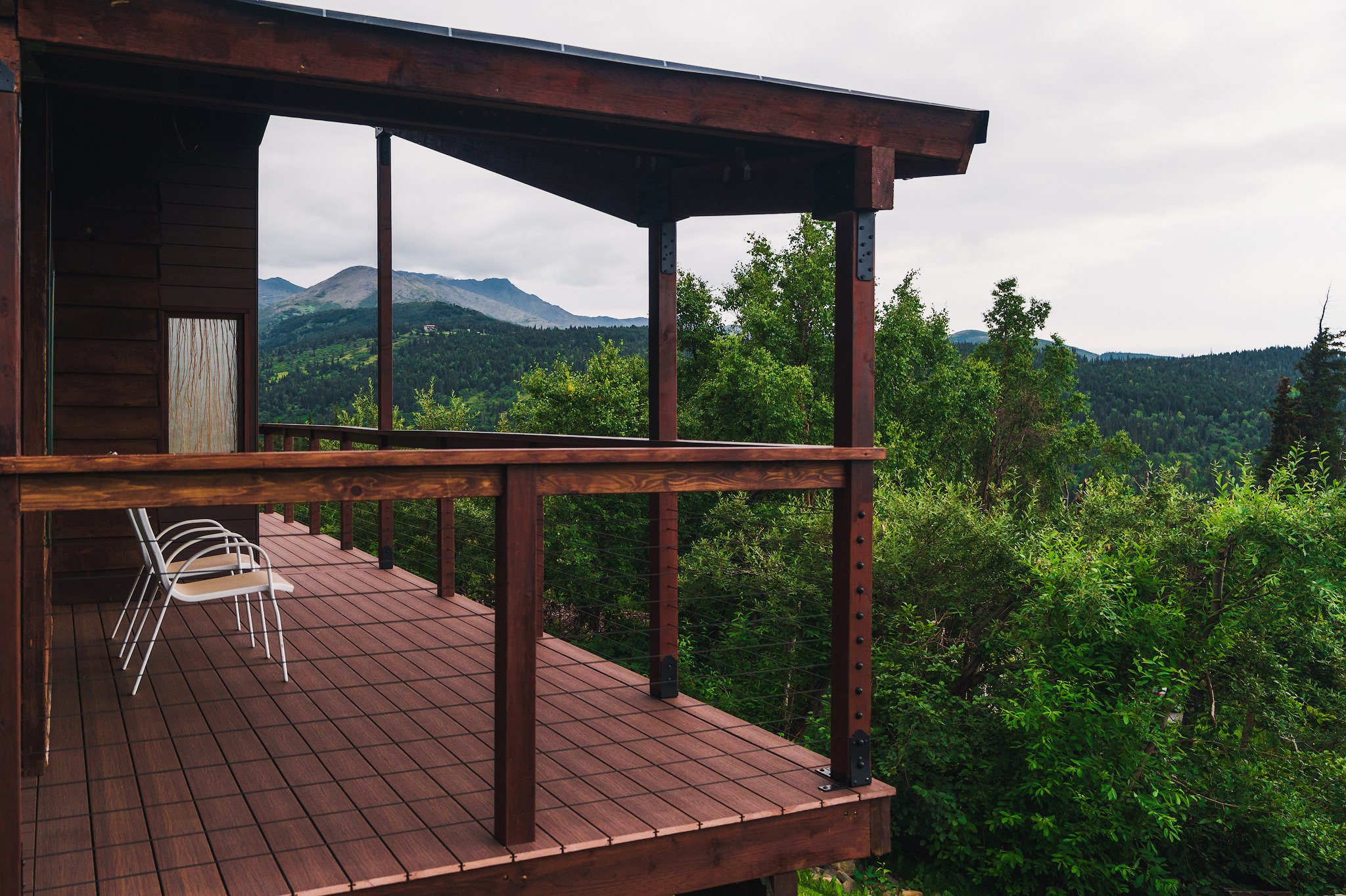 Composite decking balcony overlooking lush green trees and mountains in the distance under a cloudy sky.