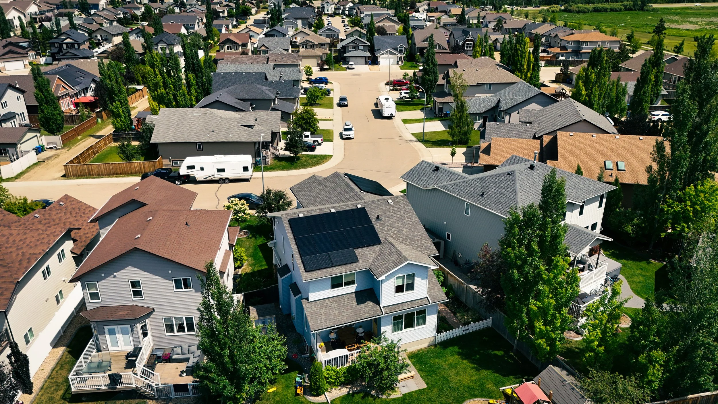Aerial view of a suburban neighborhood with houses, trees, and parked cars along streets