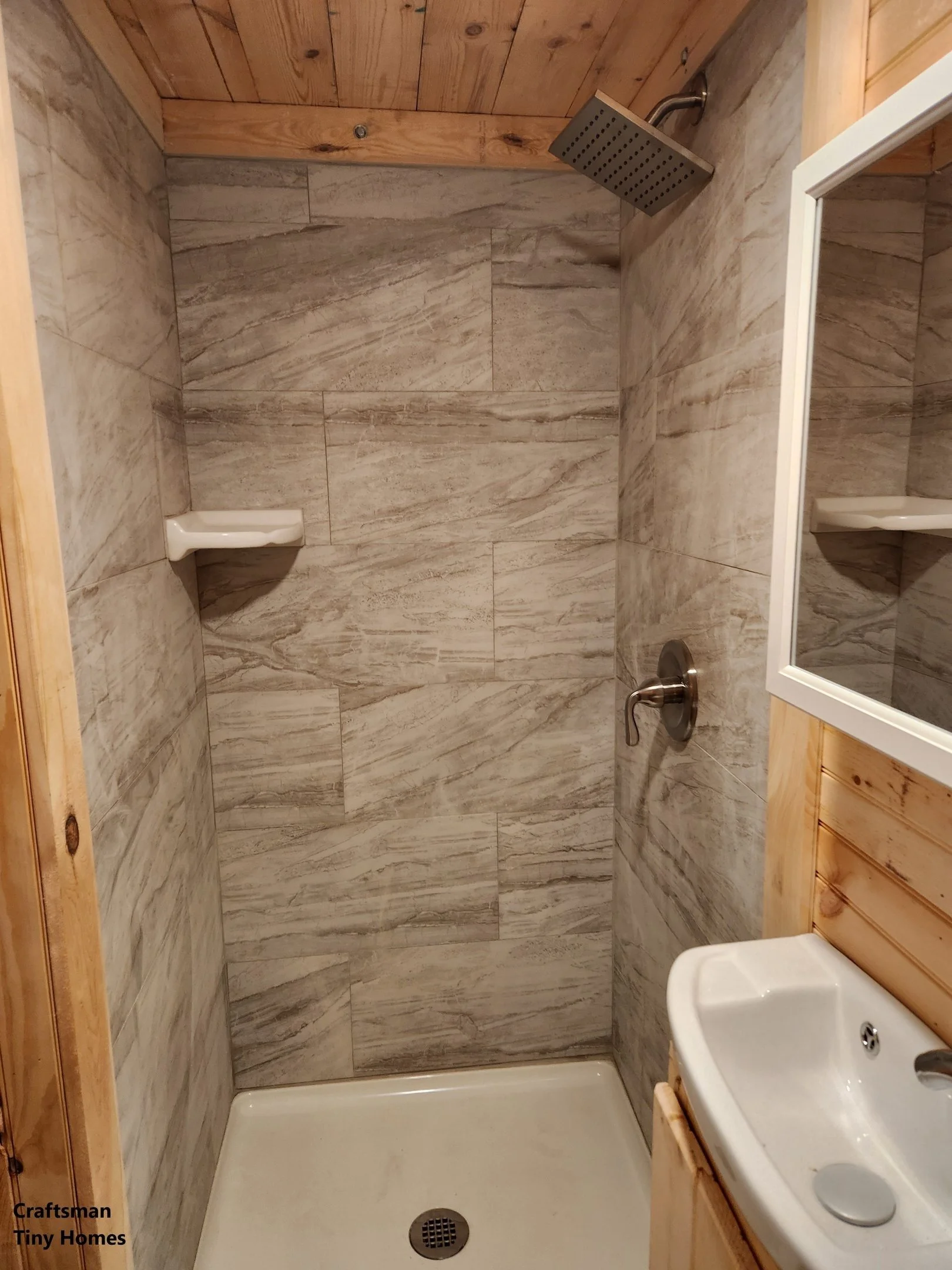 Small rustic bathroom with a walk-in shower featuring marble tiles, a wooden ceiling, and a small white sink with a mirror.