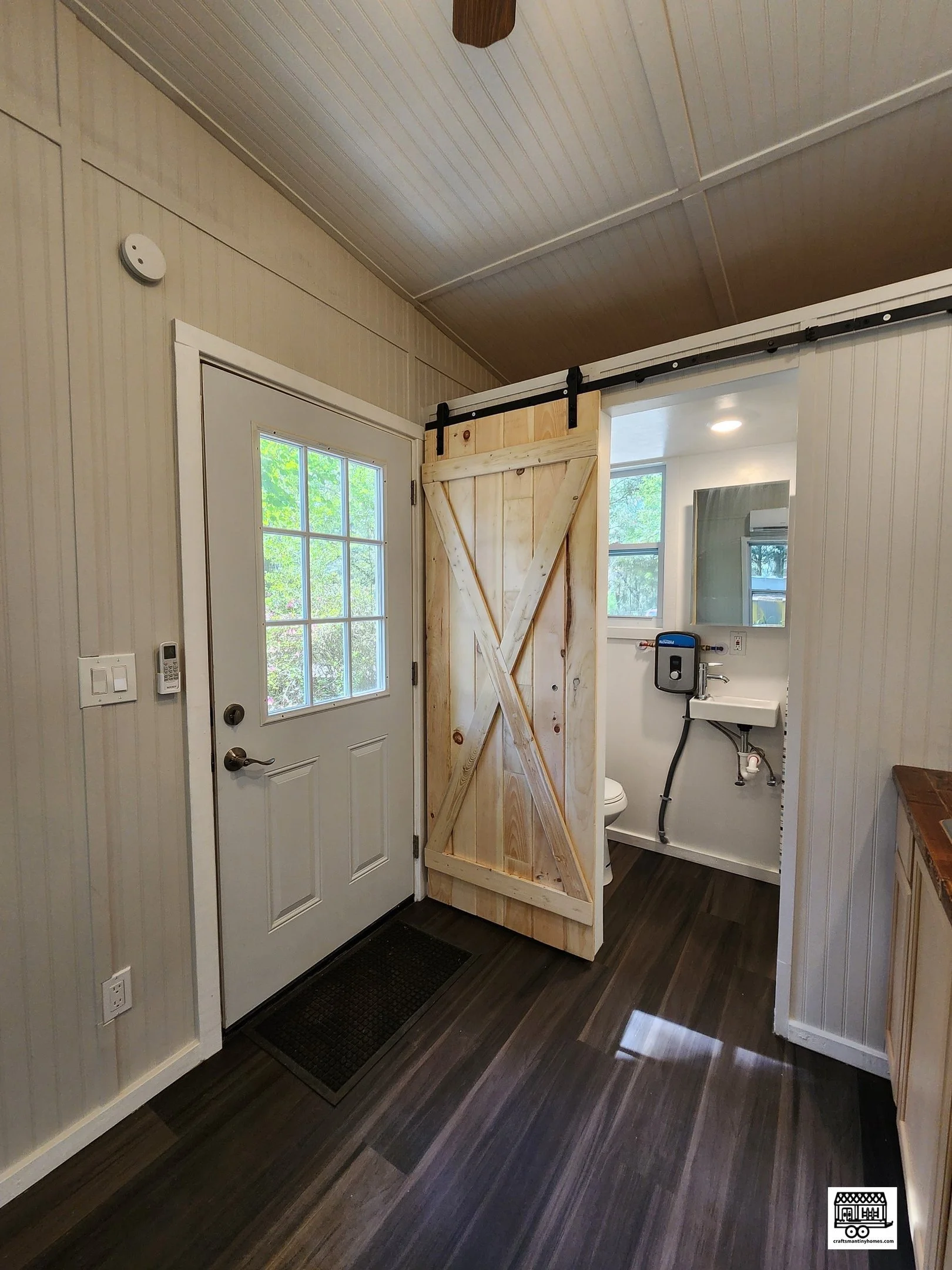 Interior of a small building with a door, a sliding barn door, and a bathroom with a toilet and small sink.