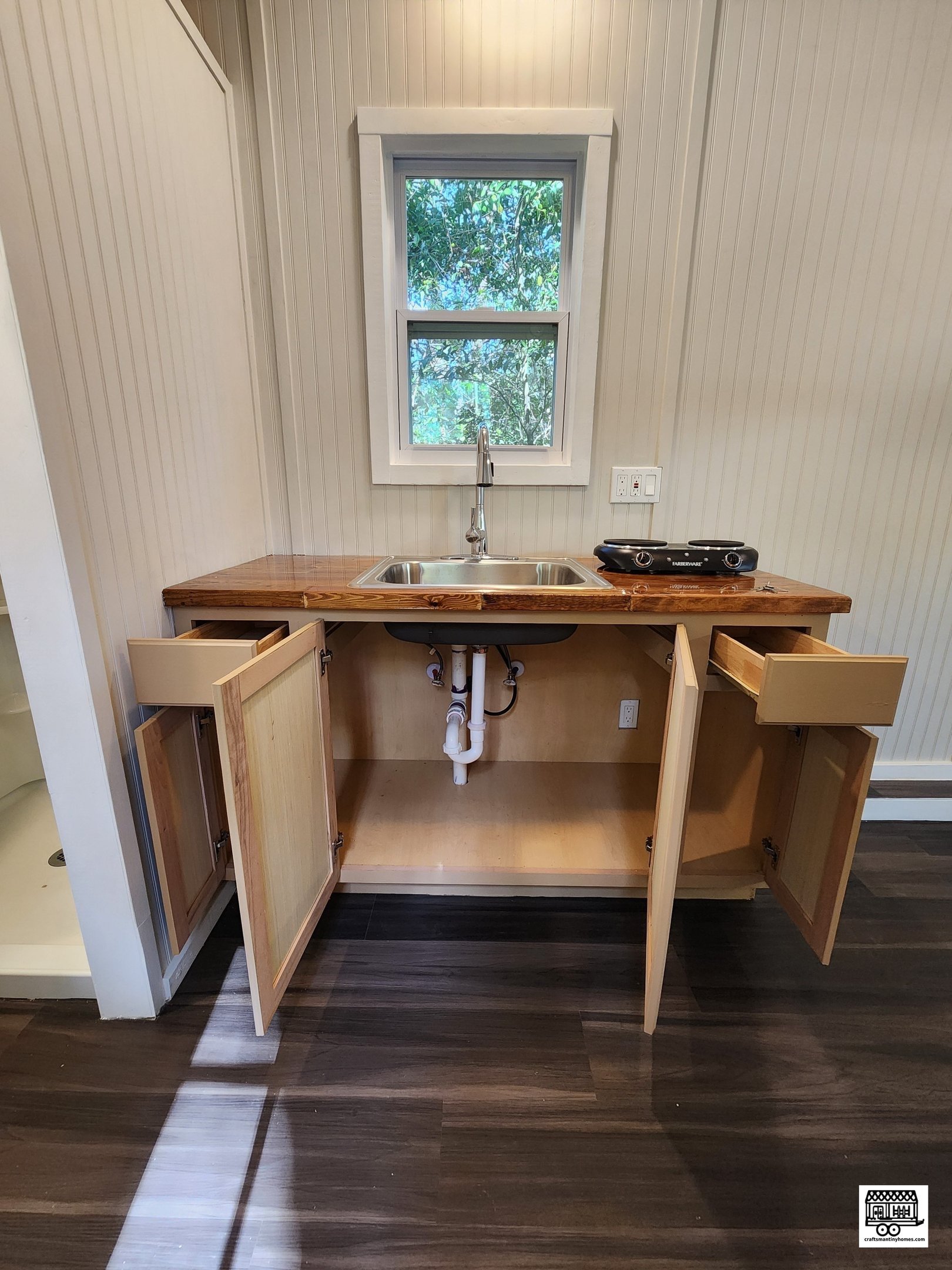 Kitchen with wooden cabinets, stainless steel sink, and window above the sink, with a small portable cooktop on the countertop.