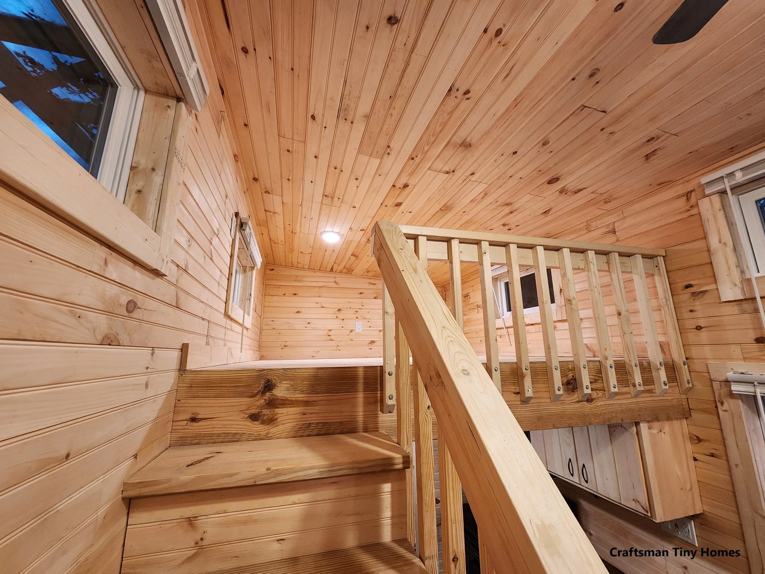Interior view of a wooden staircase, railing, and walls, with small windows and ceiling light