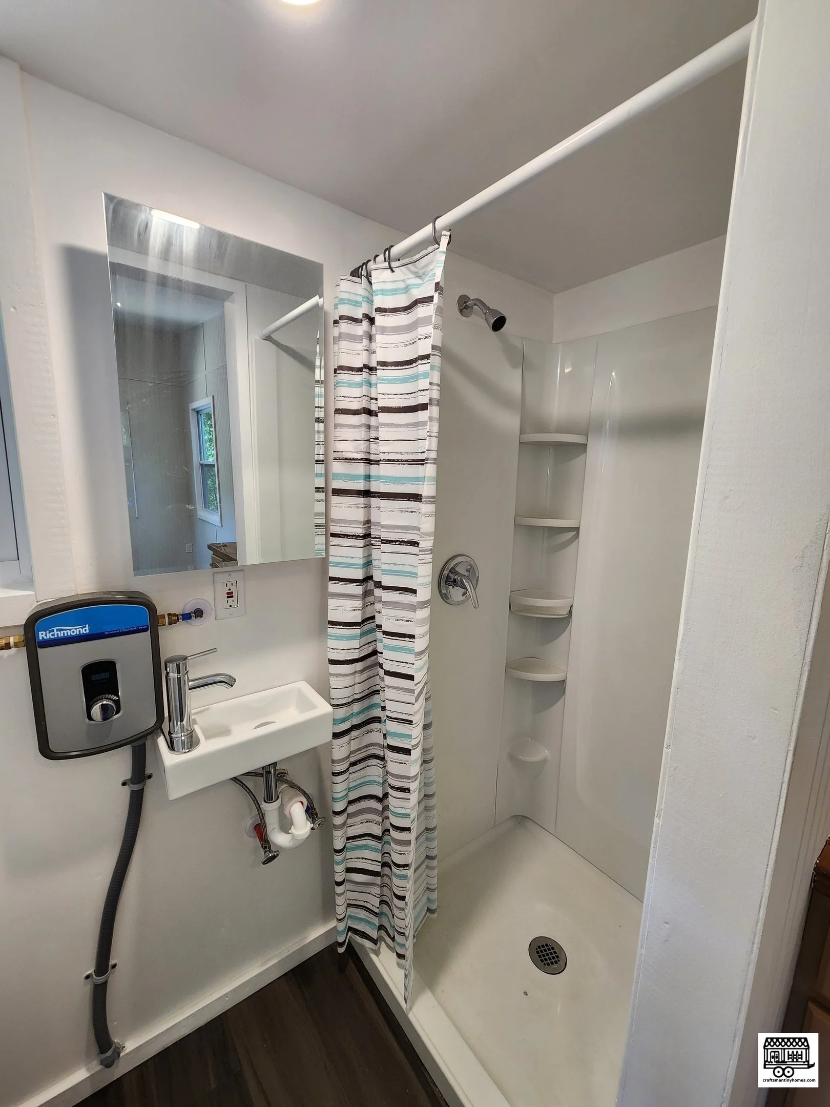 Small bathroom with walk-in shower, striped shower curtain, wall-mounted mirror, small wall-mounted sink with a hand soap dispenser, and a suction-cup storage corner in the shower.