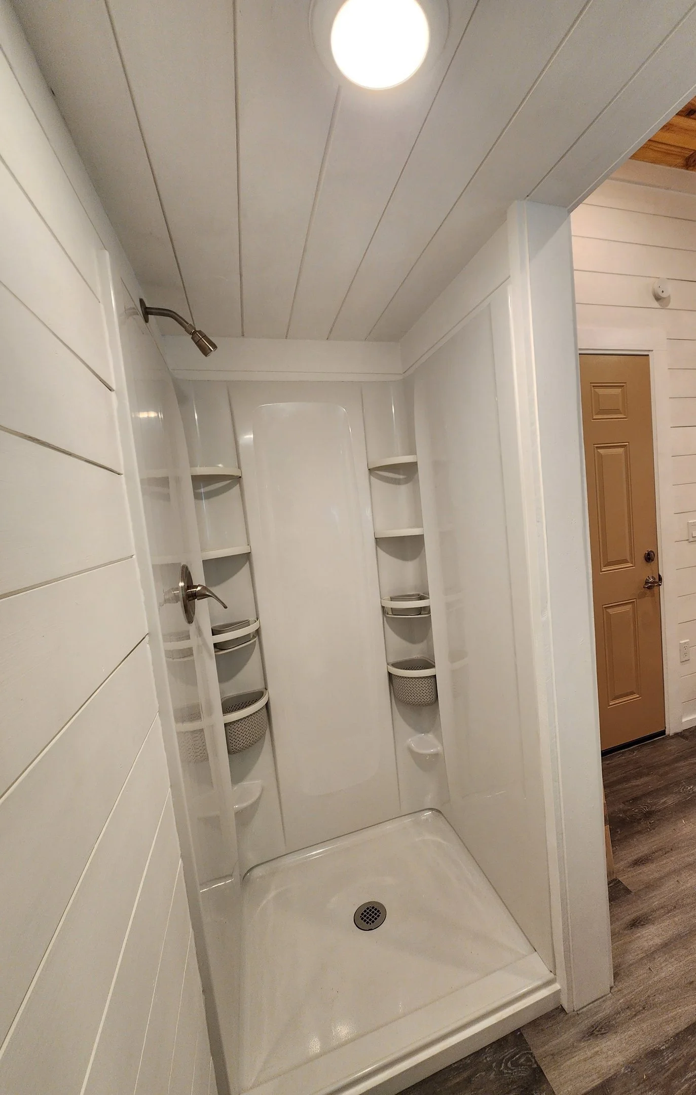 Empty white shower stall with built-in shelves and a showerhead on the left side in a bathroom.