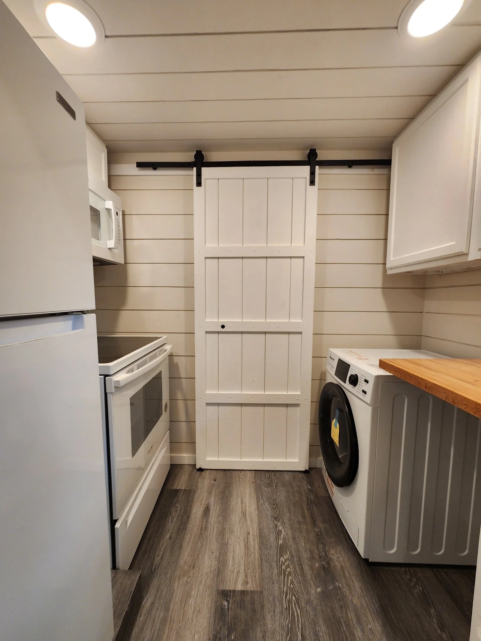 Laundry room with white appliances, wooden countertop, shiplap walls, and a sliding barn door on a black rail.