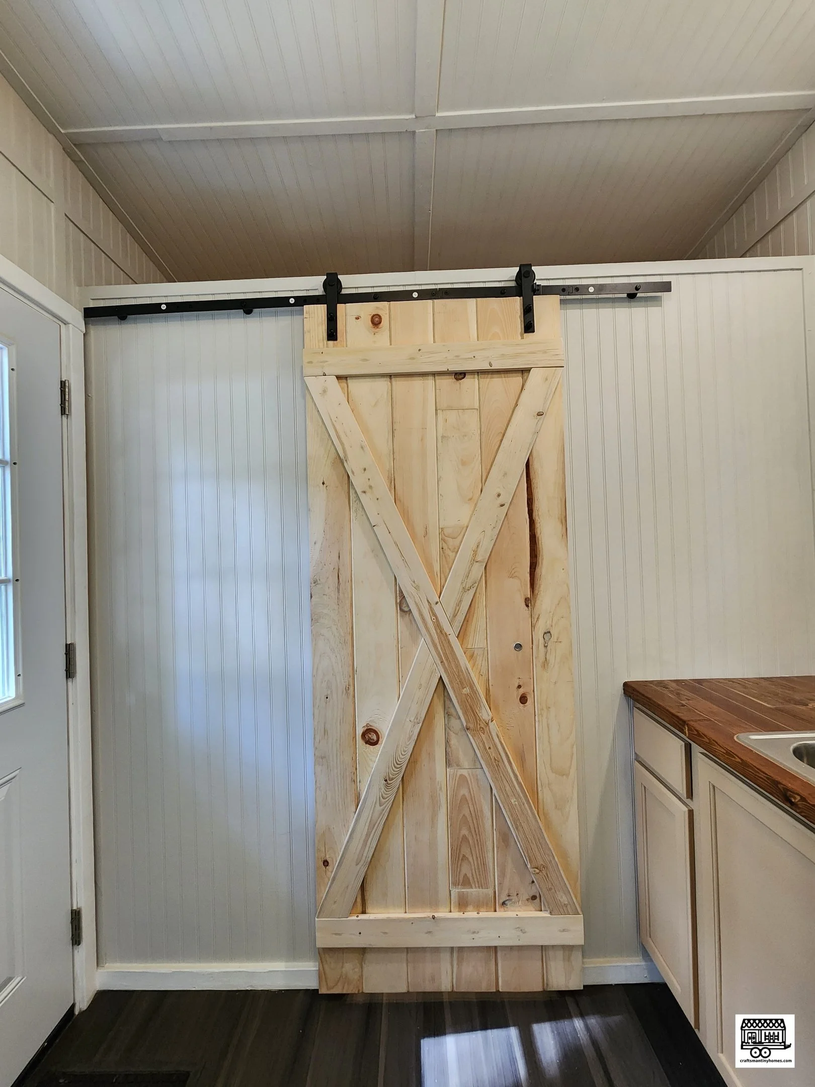 A sliding barn door mounted on a rail system, partially open, in a home interior with white walls and a wood countertop.