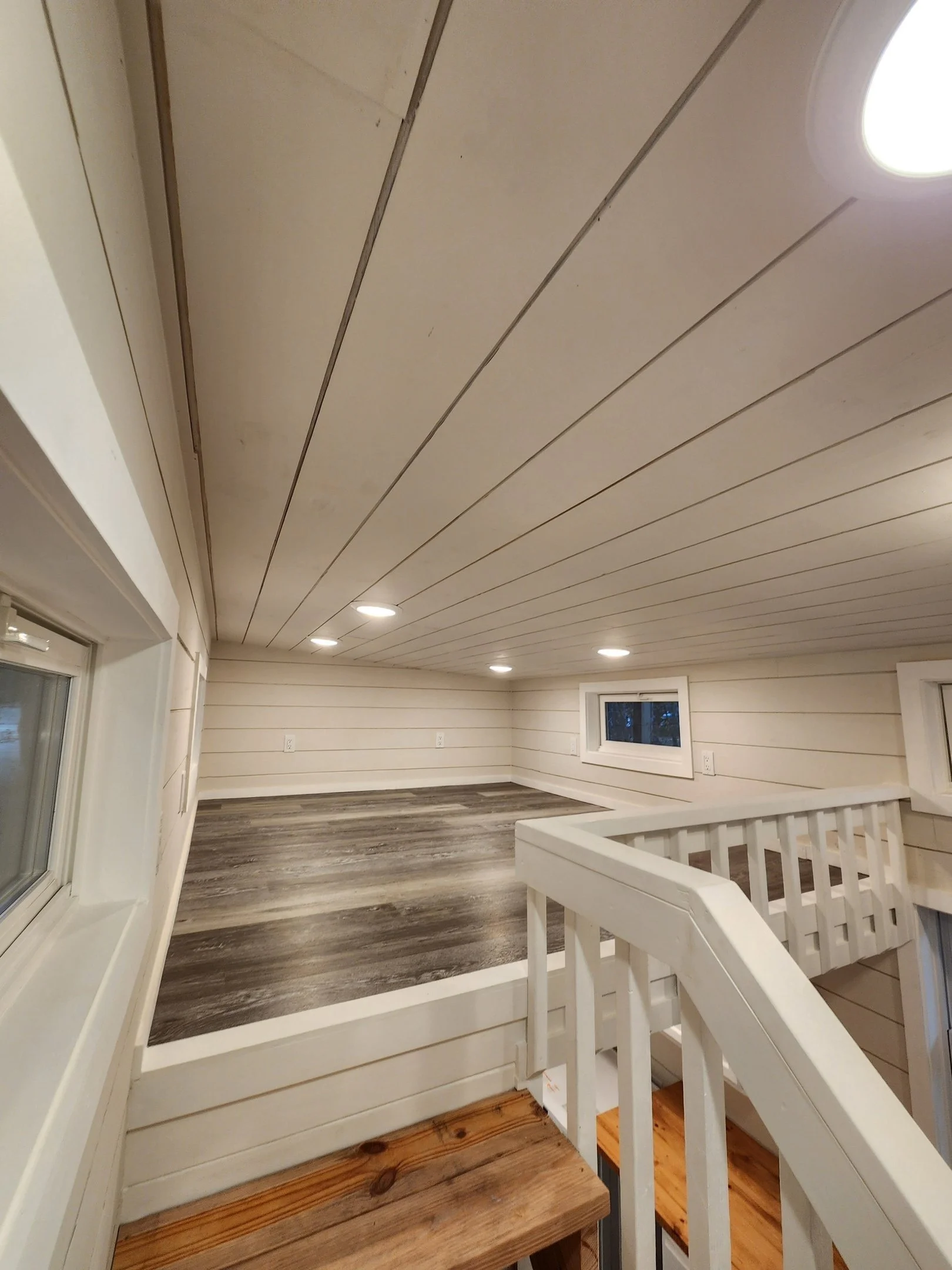 An indoor space with a sloped ceiling, white wooden paneling, recessed lighting, and a small window.