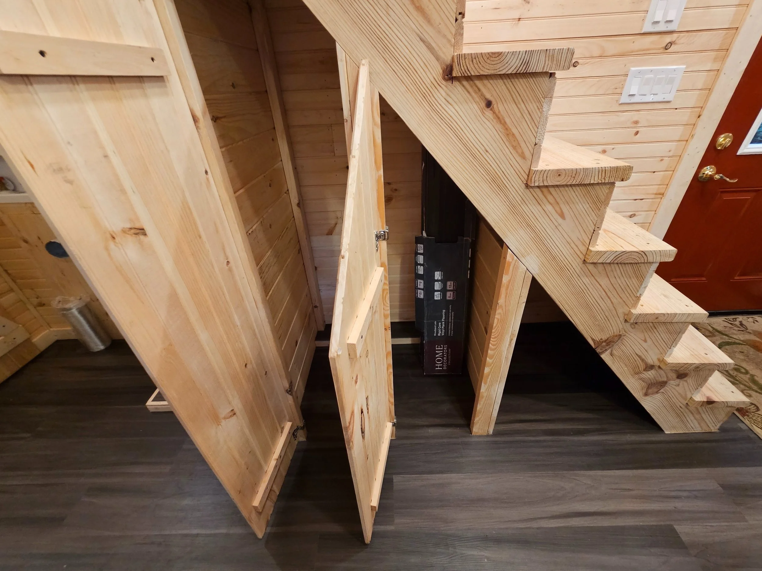 Wooden staircase with steps and handrail in a room with wood-paneled walls, partially built with tools or boxes underneath.