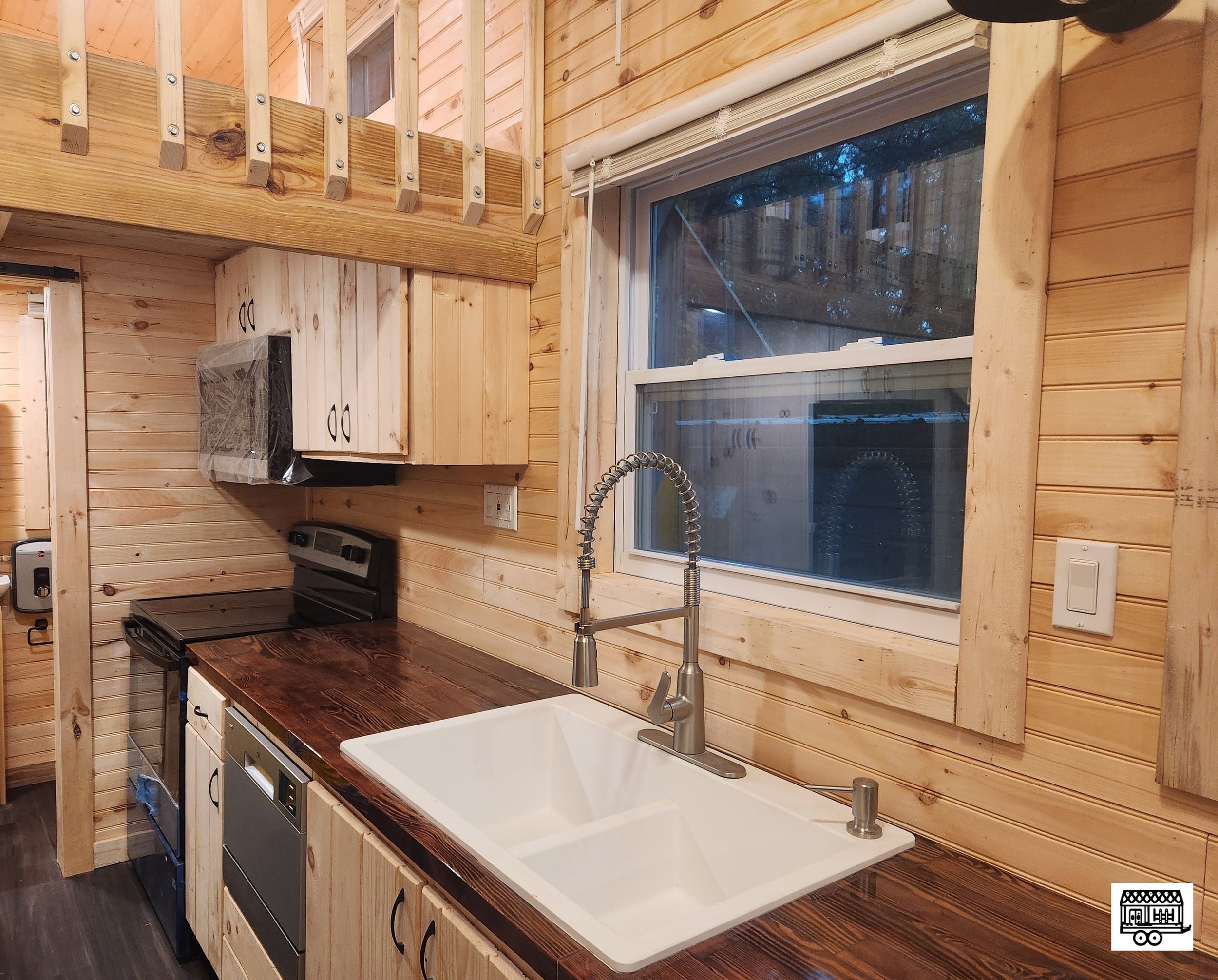 Wooden kitchen interior with a large window, sink, faucet, stove, and cabinetry in a log cabin style.