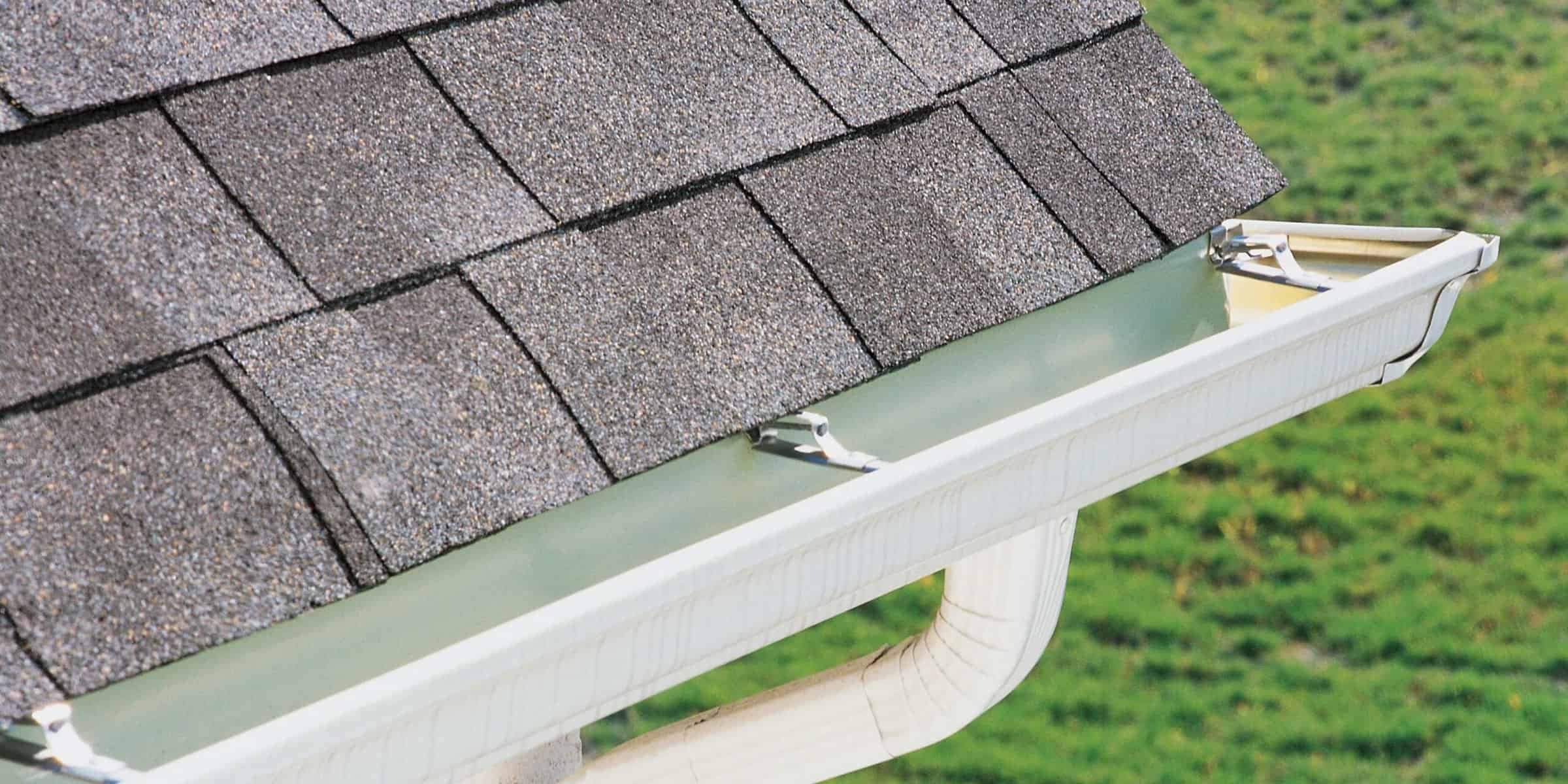 Close-up of a residential roof with asphalt shingles and a new clean white gutter system.
