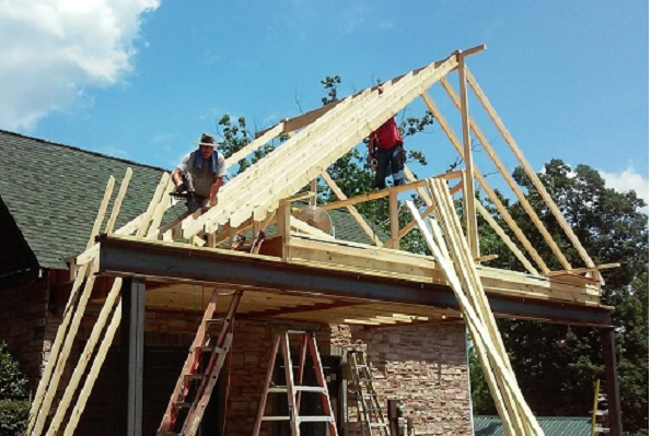 Two construction workers installing a roof frame on a house with wooden beams, ladder.