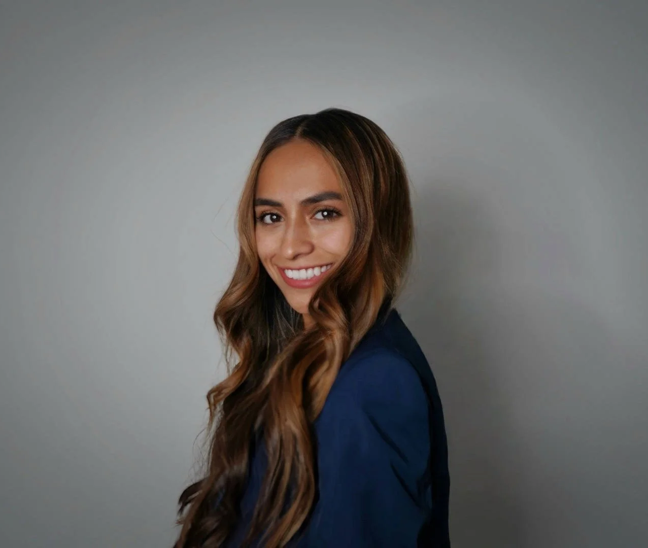 Crystal smiling at the camera, wearing a navy blue blazer against a plain gray background.