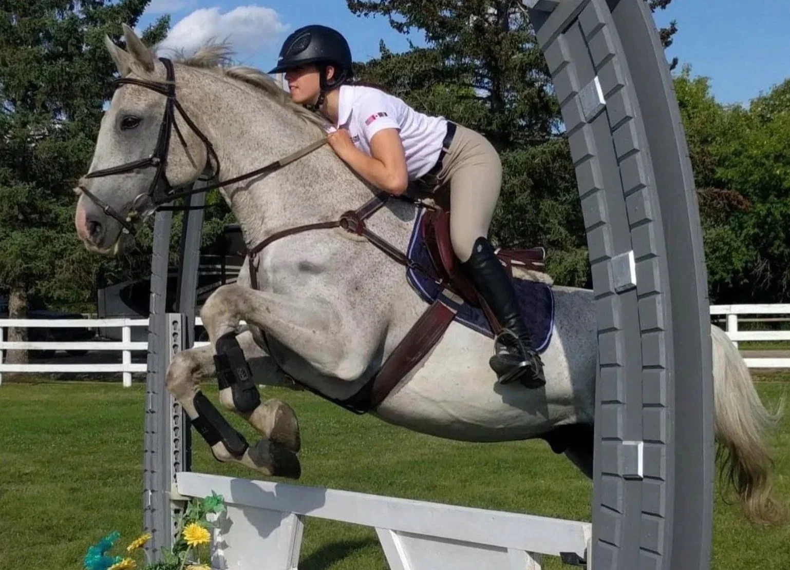 A woman riding a white horse while jumping over a hurdle during an equestrian event.