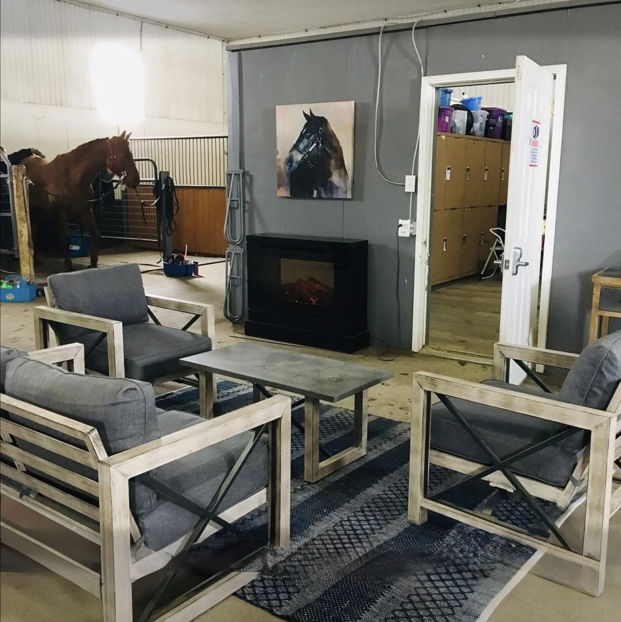 Photo of a room with wooden and metal furniture, a painting of a horse on the wall, a fireplace, and a closet with plastic containers on top.