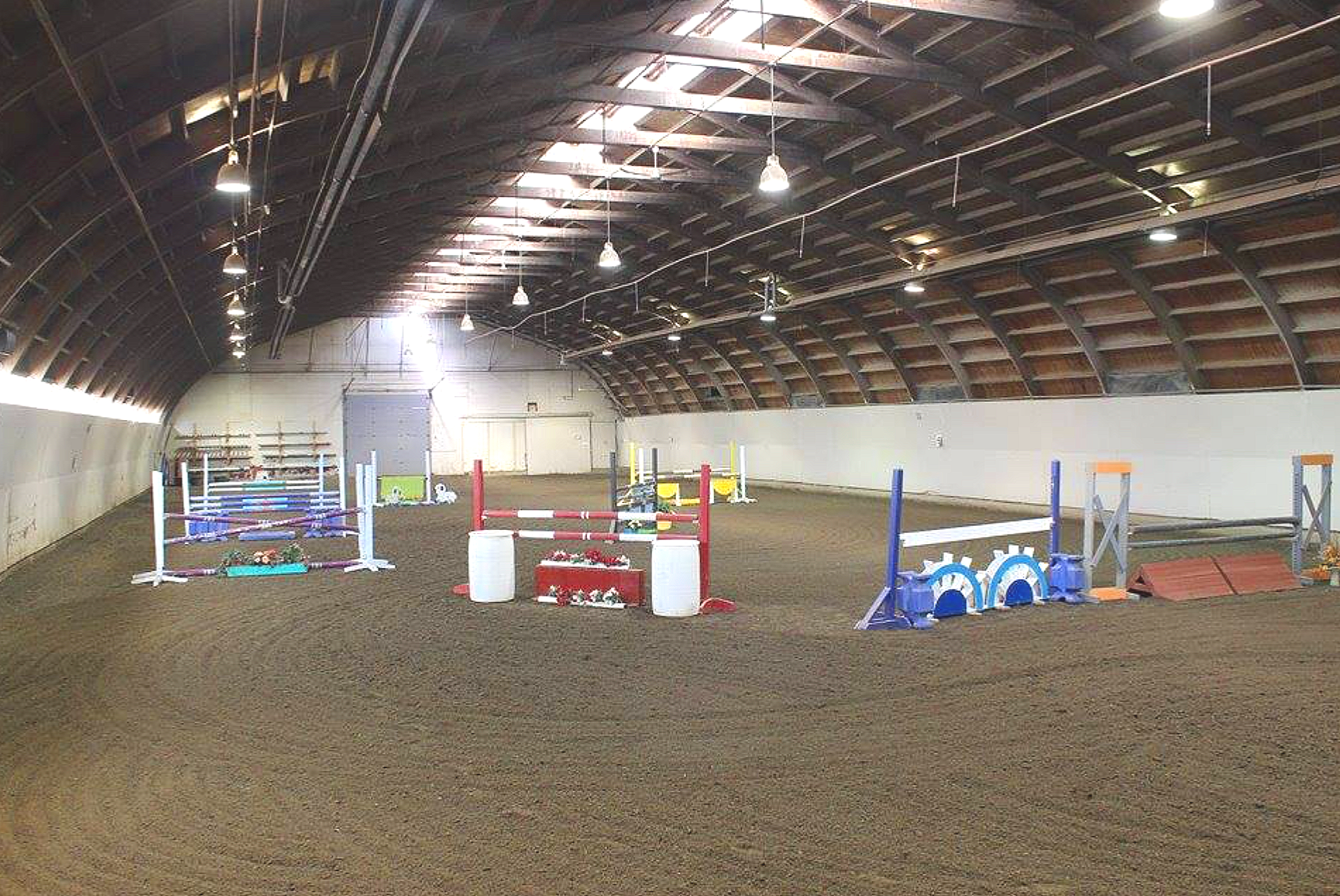 Indoor horse riding arena with colorful jumps and obstacles for training.