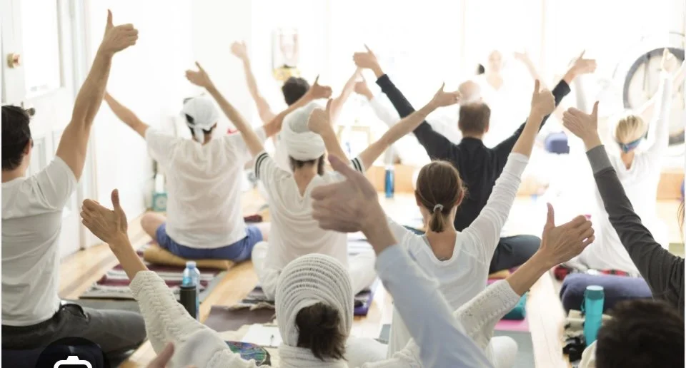 Group of people participating in a yoga or meditation class, sitting on mats with arms raised in a relaxed pose.
