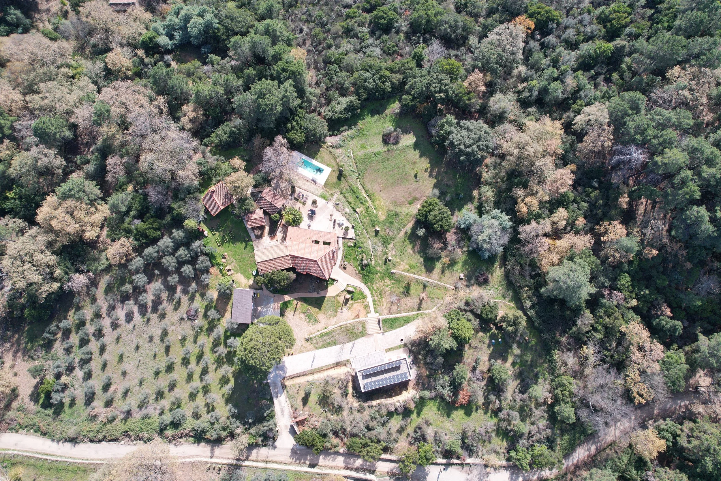 Vista aérea de una casa en medio de un bosque con piscina, caminos y áreas verdes.