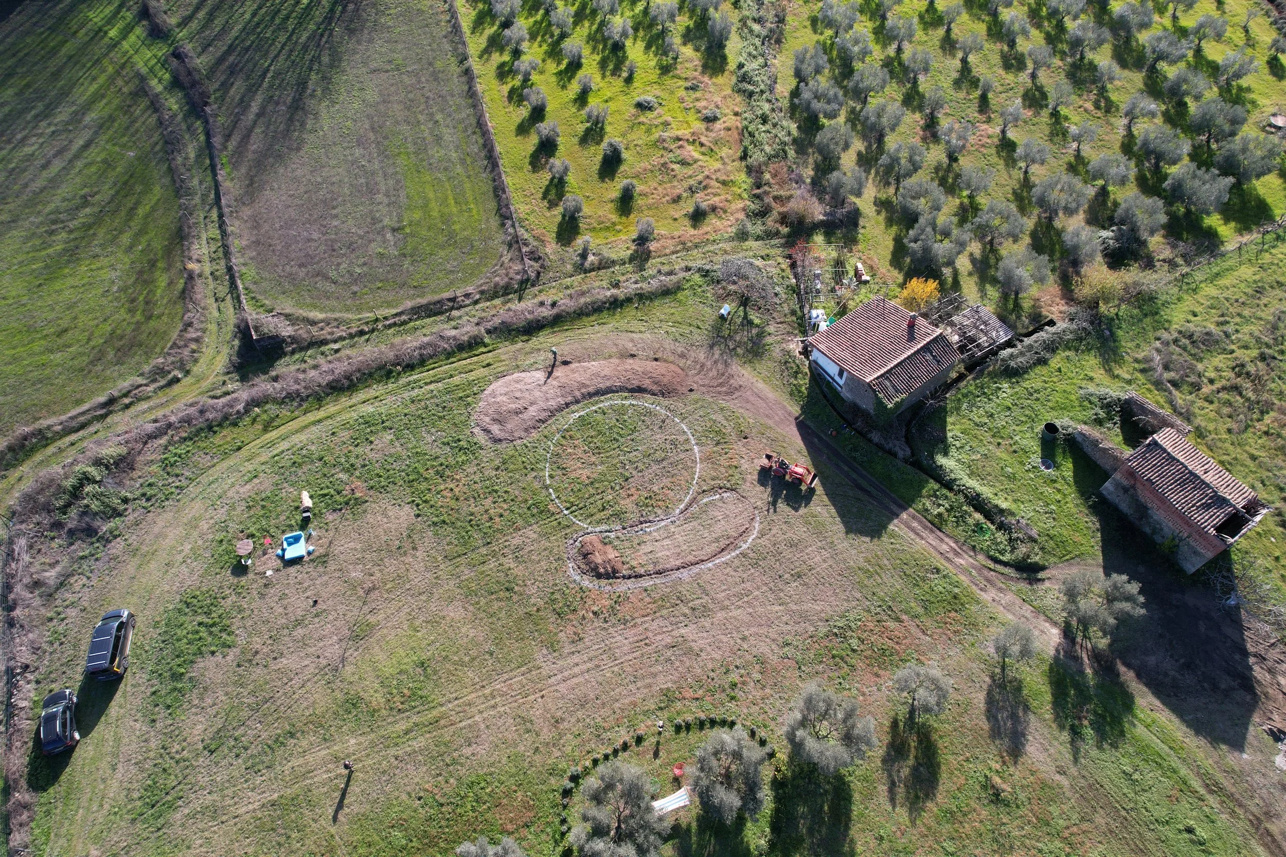 Vista aérea de un patio rural con casas, árboles, un campo de juegos improvisado con círculos de cuerda, y vehículos en la zona