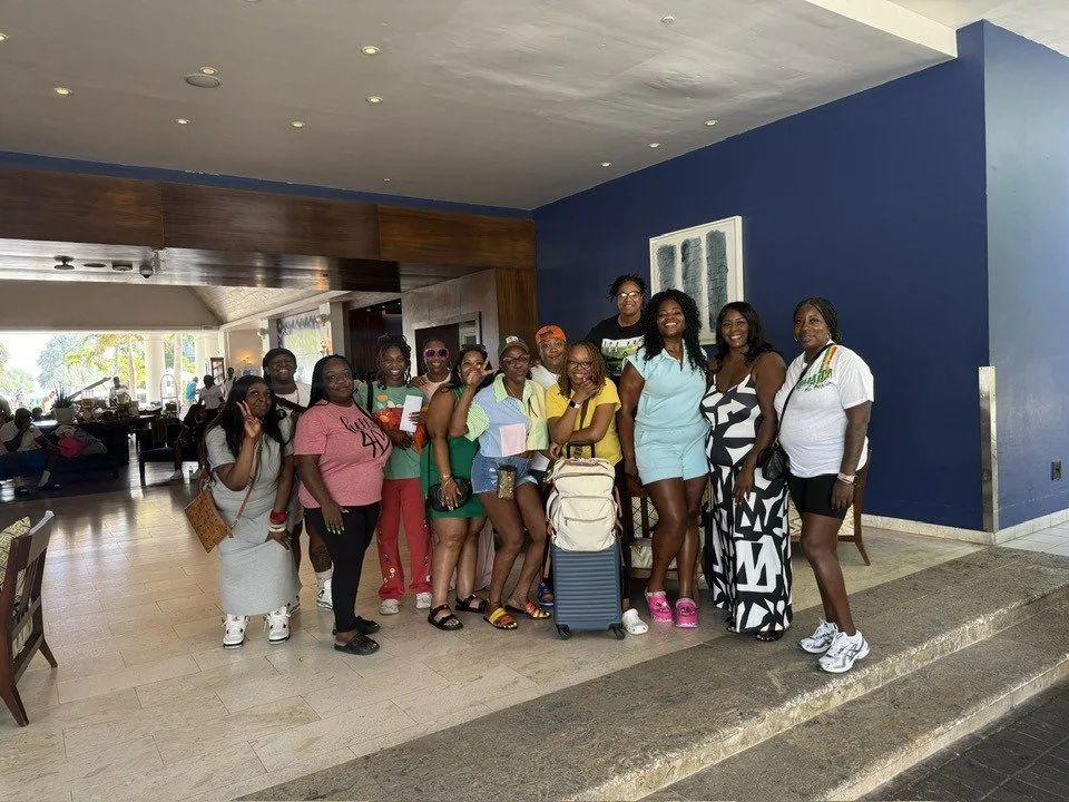 A group of women and girls are standing together inside a hotel lobby, smiling for a photo, with some luggage in front of them.