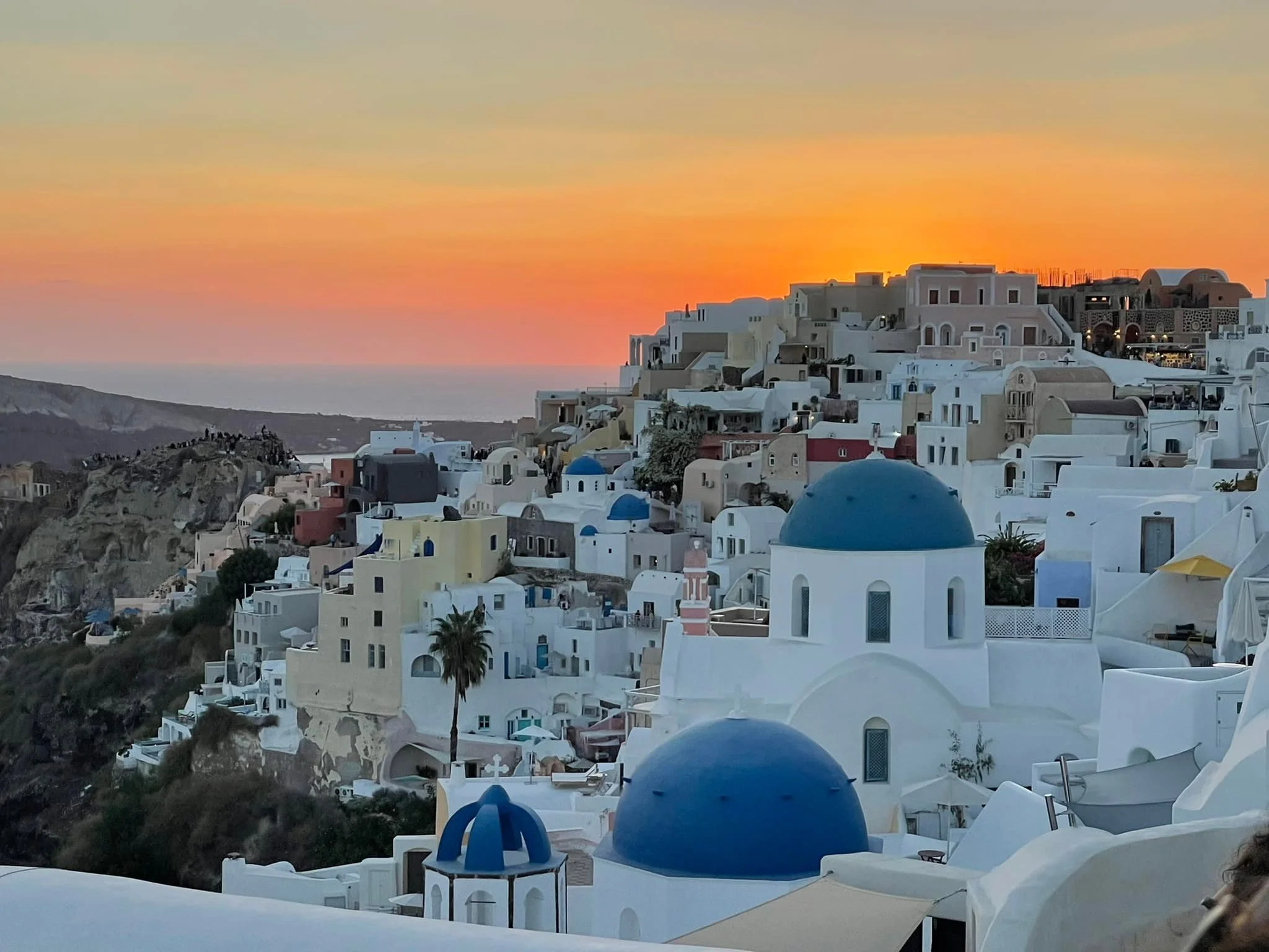Sunset over the hillside of Santorini, Greece, with white buildings and blue-domed churches.