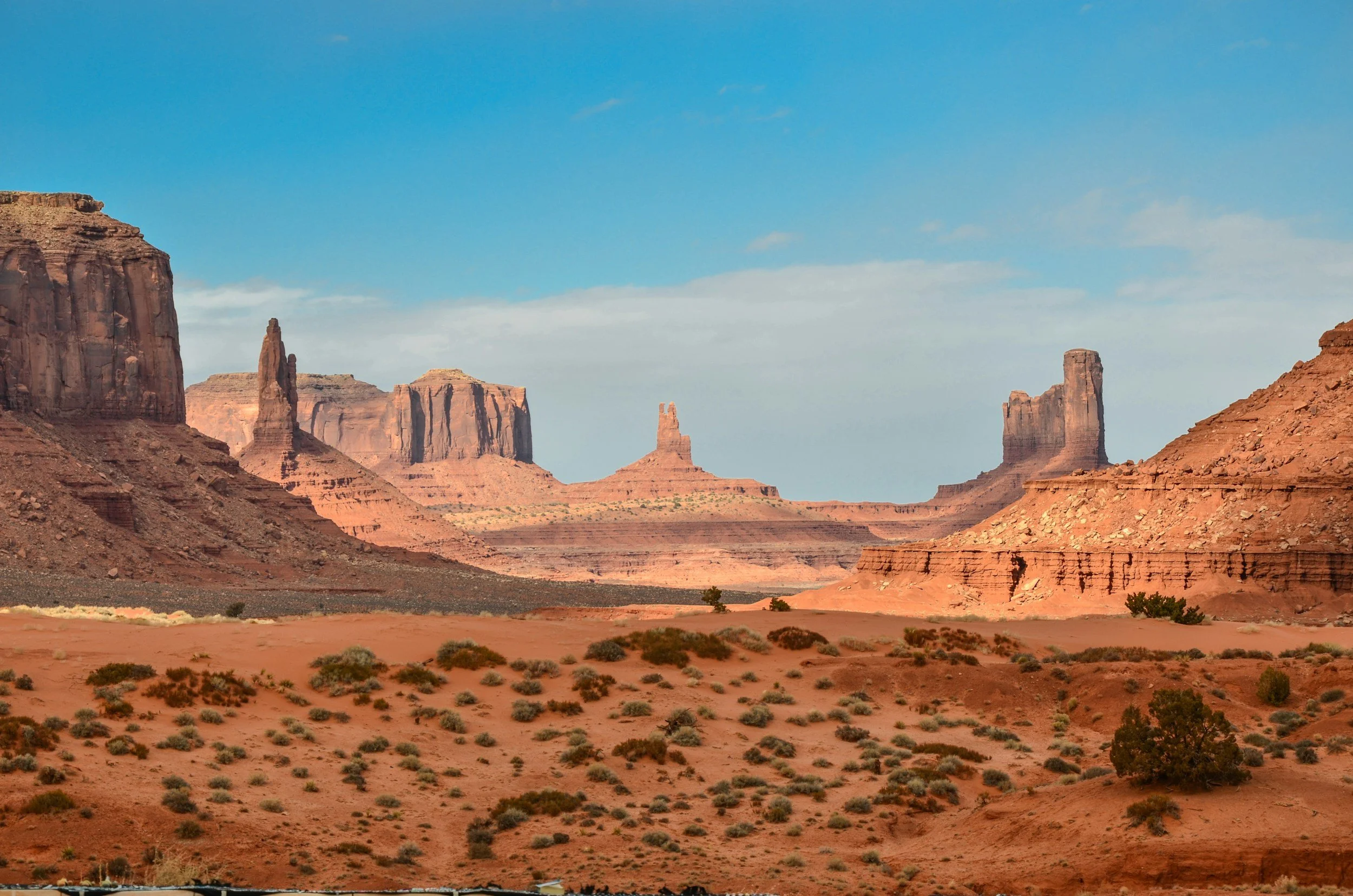 Desert landscape with large sandstone formations and sparse vegetation under a partly cloudy sky.
