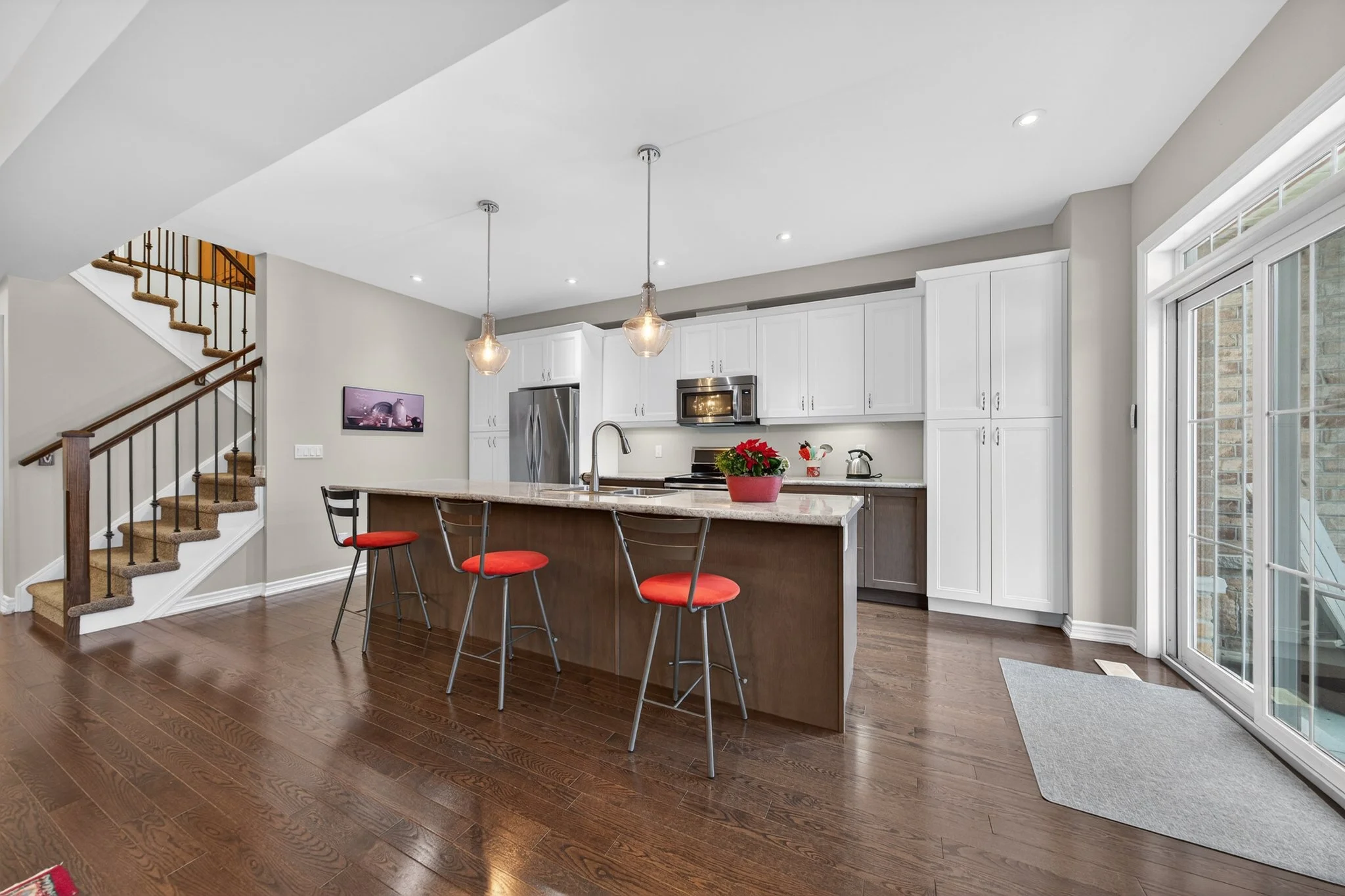 Modern kitchen with white cabinets, stainless steel appliances, and a wooden island with red barstools. Bright and spacious, featuring sliding glass doors and hardwood floors.