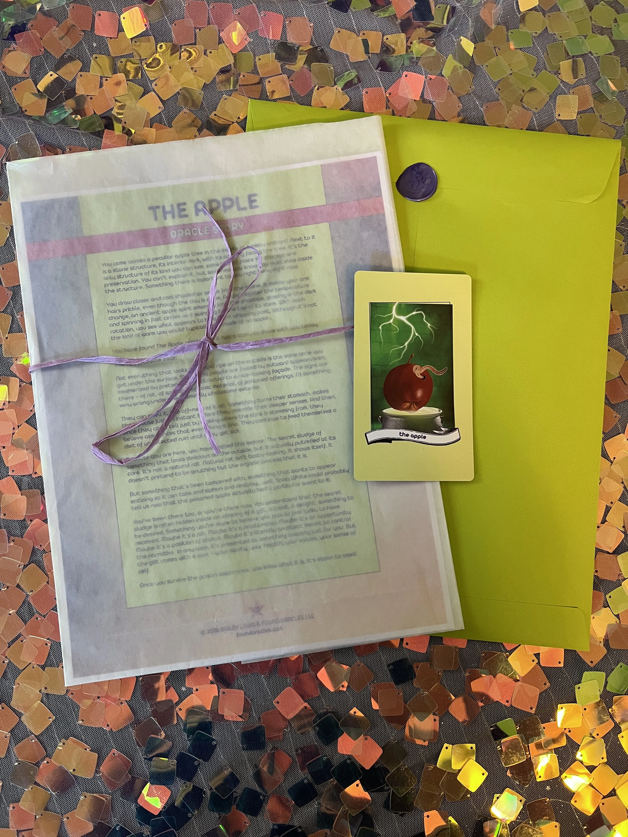 Flat lay shot of The Apple printed story card and story sheet from Found Oracles with purple wax sealed green envelope behind.