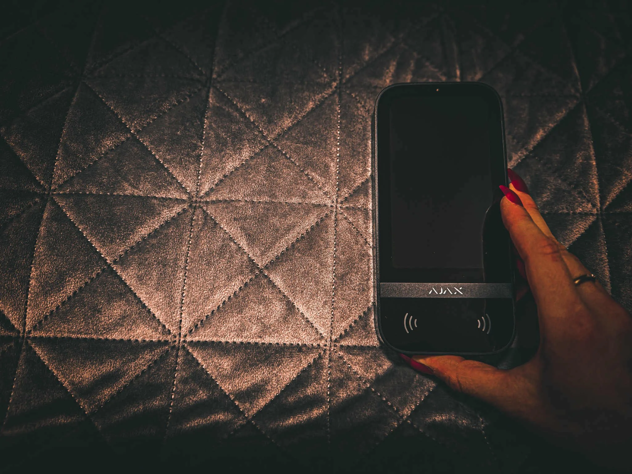 Person holding a black contactless payment device over a textured, quilted surface.