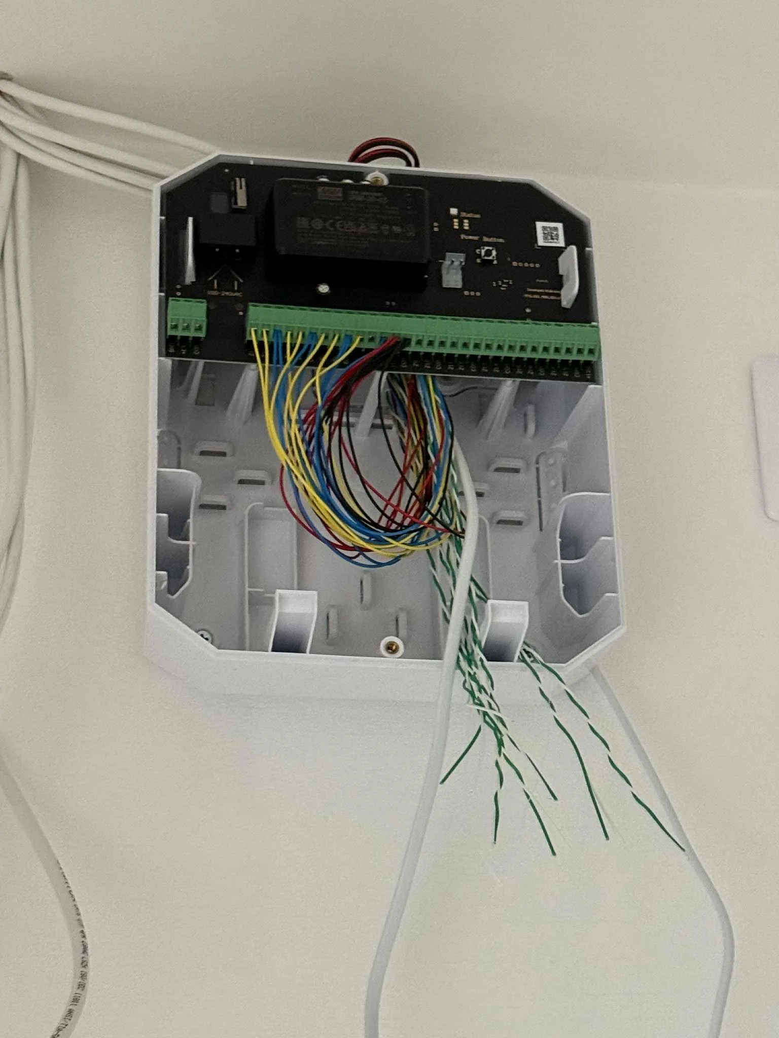 An open electronic control panel with colorful wires hanging inside a white enclosure, mounted on a wall, with a circuit board and components visible.