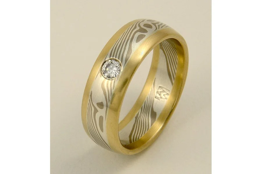 I helped a client design this ring as a memorial to his recently departed wife. The side bands of yellow gold are their actual wedding rings they wore for 37 years, melted down and forged anew. Material is 14k palladium white gold and sterling silver
