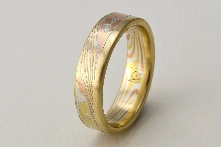 Kaze (Wind) ~ Swirling lines of mokume resemble the path of a breeze moving through trees. One solid edge of gold (rose, yellow or white) calms and anchors the design. Available from 5 to 8mm wide. This selection is sterling silver, 18k yellow gold a