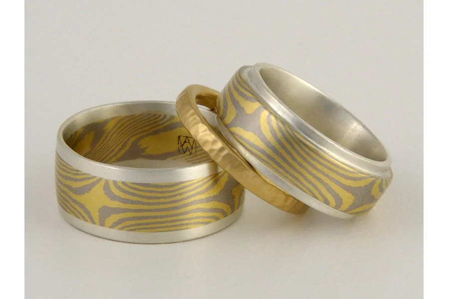 Custom color combination: 18k yellow gold and 950 palladium mokume gane in a star pattern. The left ring has added sterling silver edging, while the right ring has an inner band of sterling silver. Middle ring is an 18k yellow hammered band engagemen