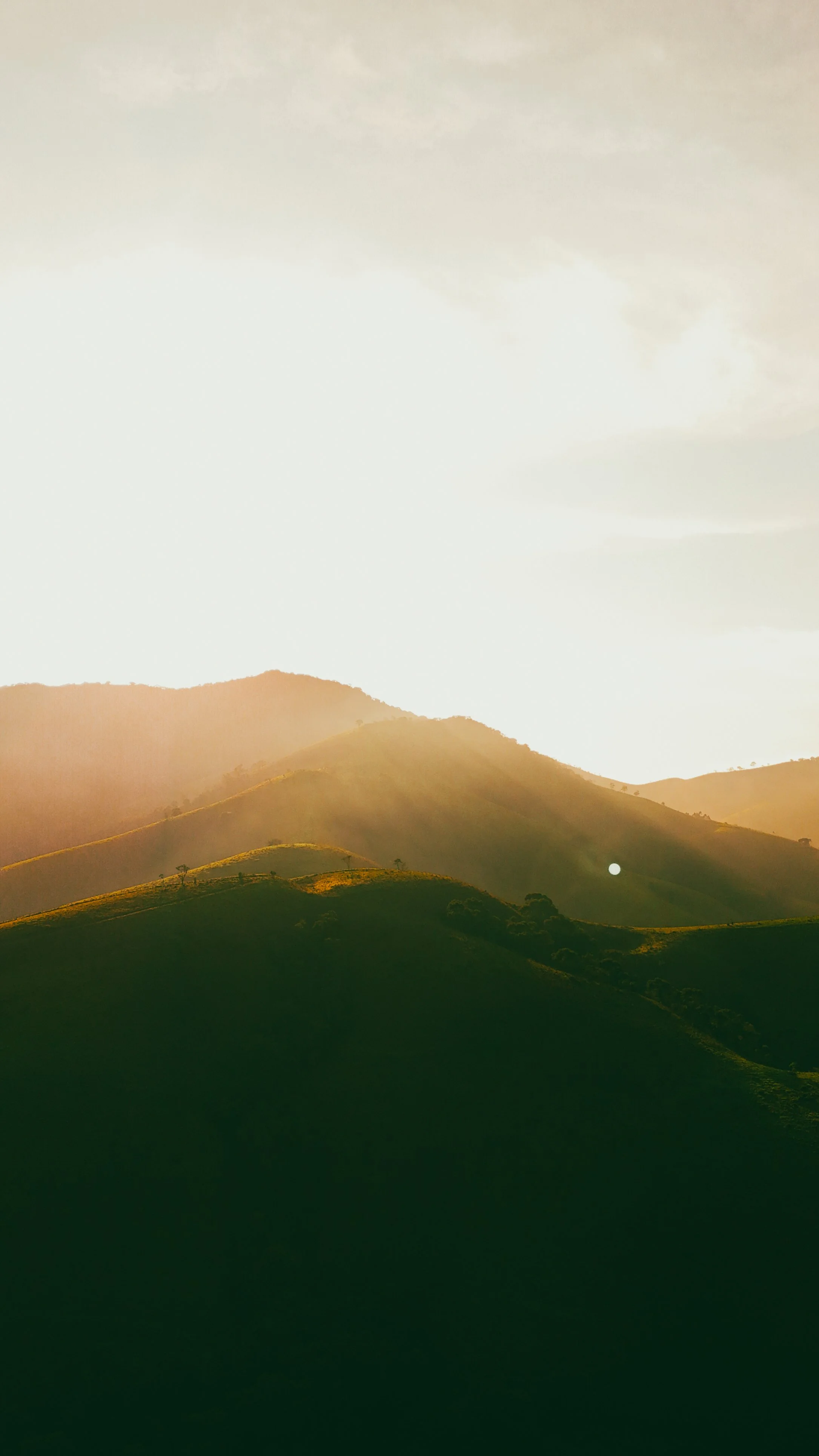 Paisagem com montanhas verdes ao pôr do sol, com céu parcialmente nublado e luz dourada refletindo nas encostas.