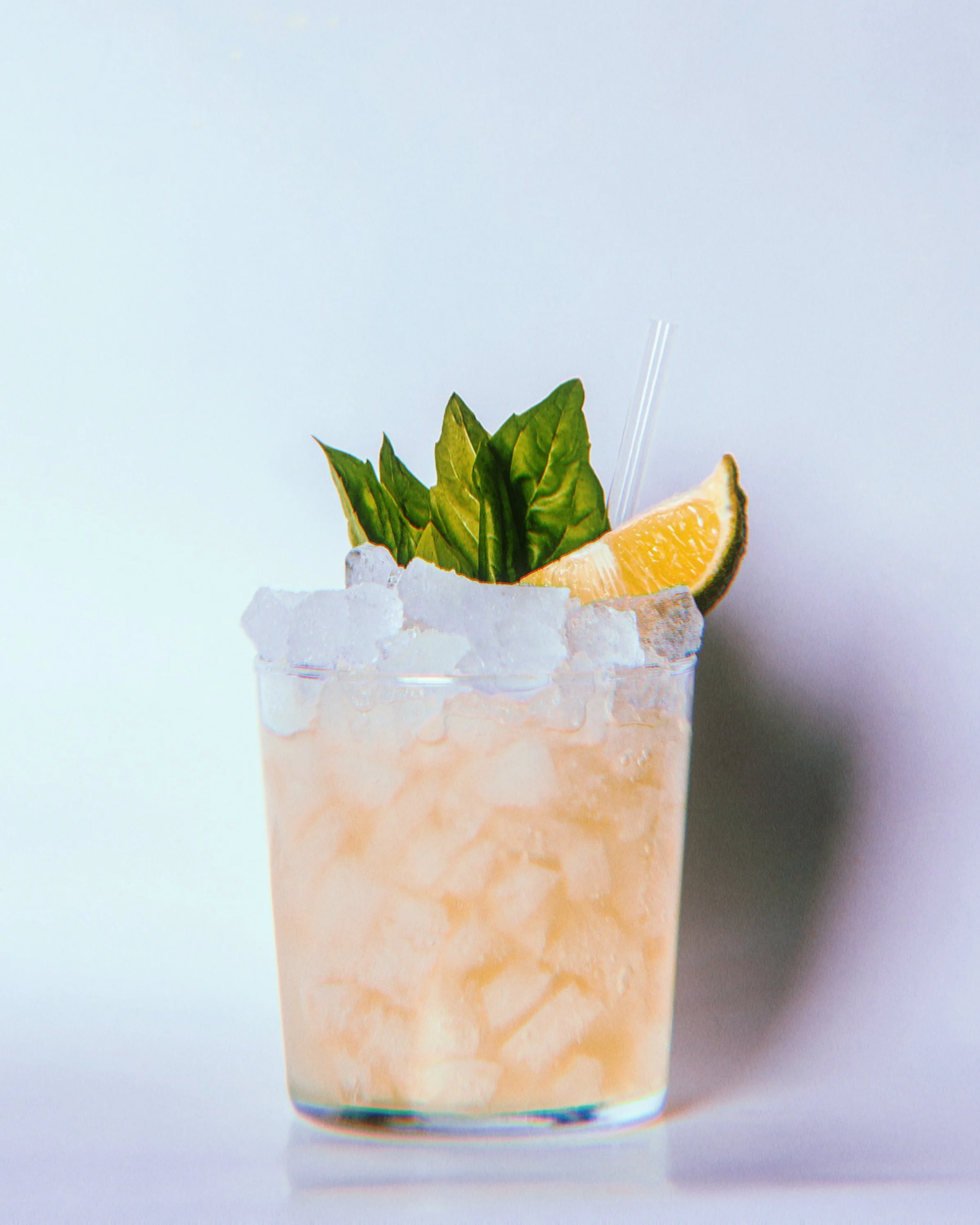 Verre de cocktail rose avec glaçons, garniture de feuilles de basilic, tranche de citron vert et une paille