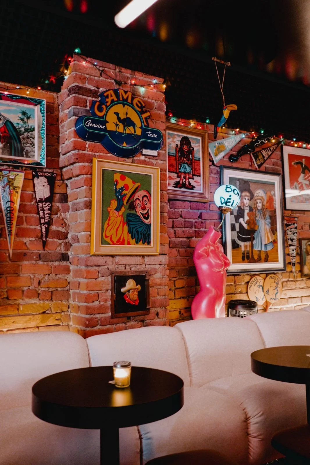 Mur en briques avec décorations variées : imagettes, enseignes, lampions, sculptures, portraits et objets décoratifs dans un intérieur de restaurant ou bar.