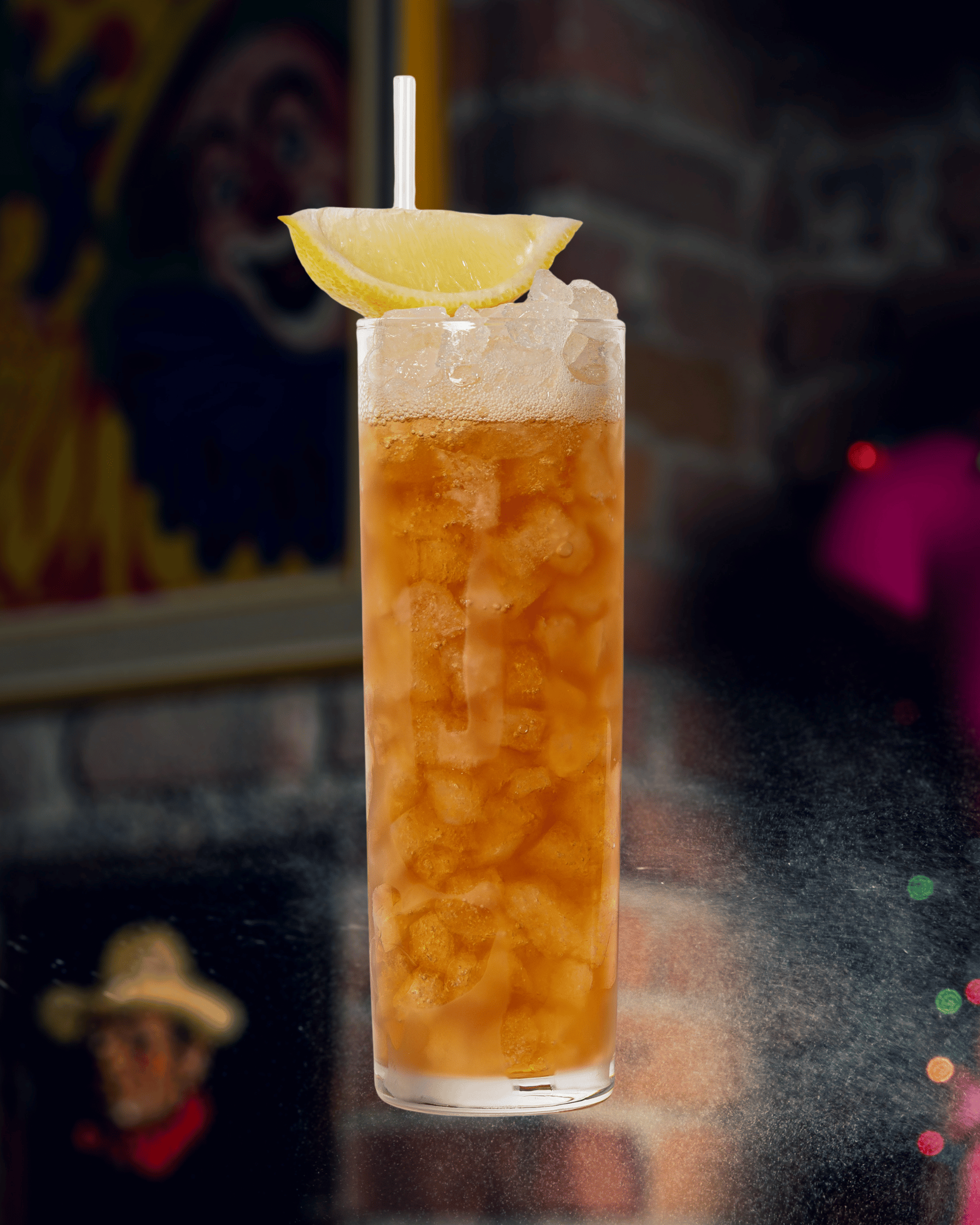 Un grand verre de boisson glacée avec une tranche de citron sur le rebord, une paille blanche, et du sirop d'orgeat, dans un décor de bar ou de restaurant.