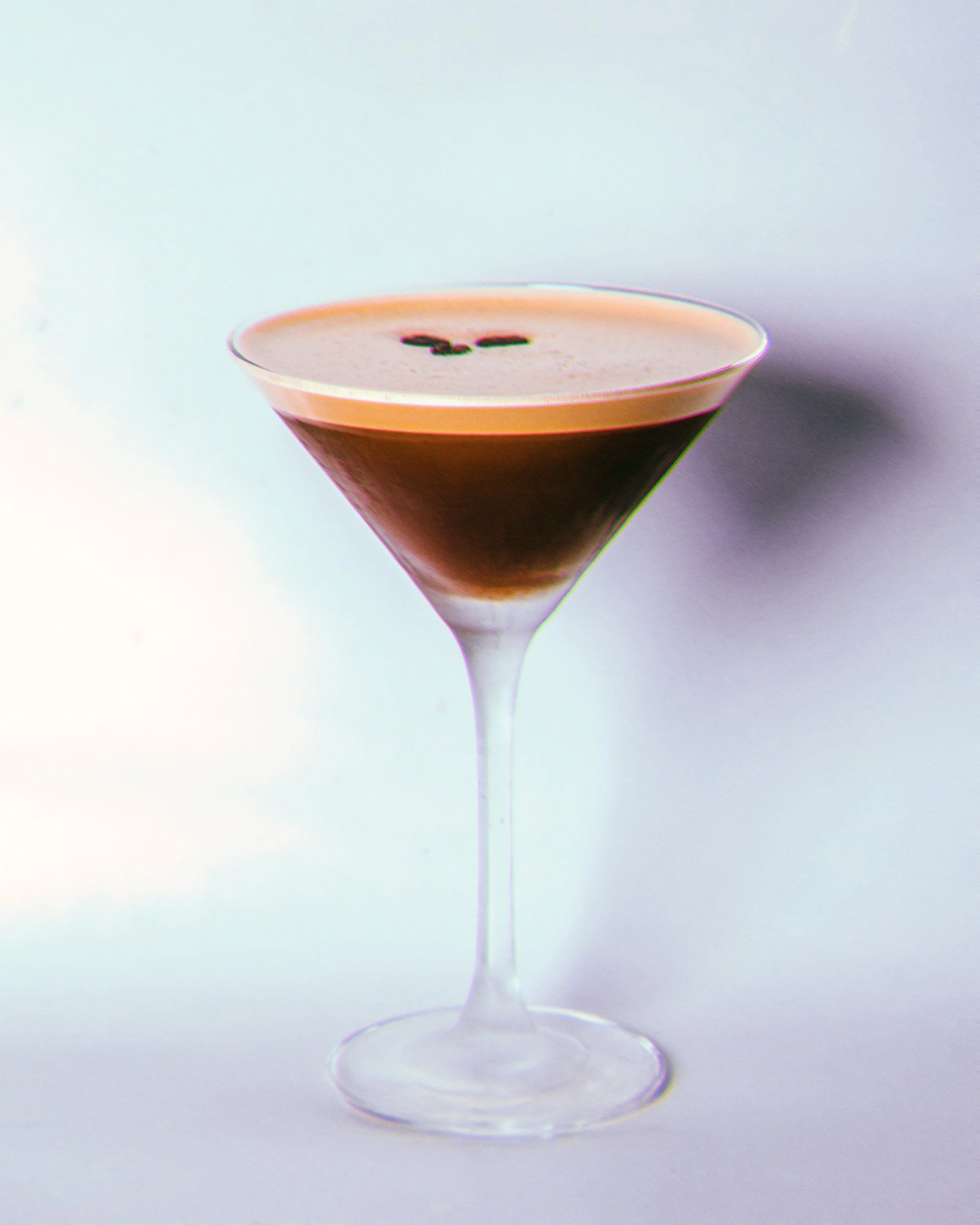 Un cocktail dans un verre à martini avec une crème au dessus, garnie de quelques grains de café.