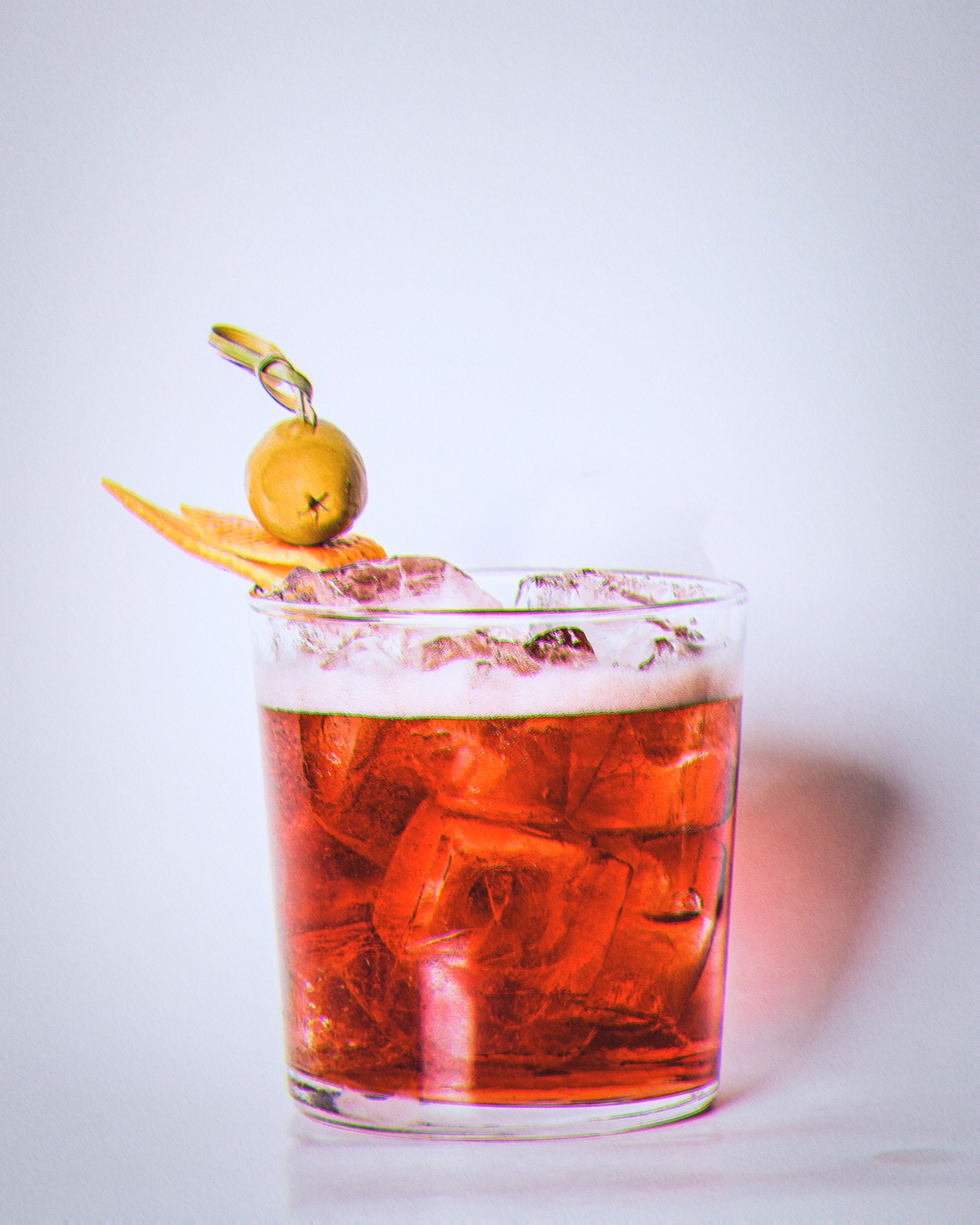 Un verre de cocktail rouge avec des glaçons, décoré d'une olive vert olive piquée sur un cure-dent, d'une tranche d'orange et d'une rondelle de citron.