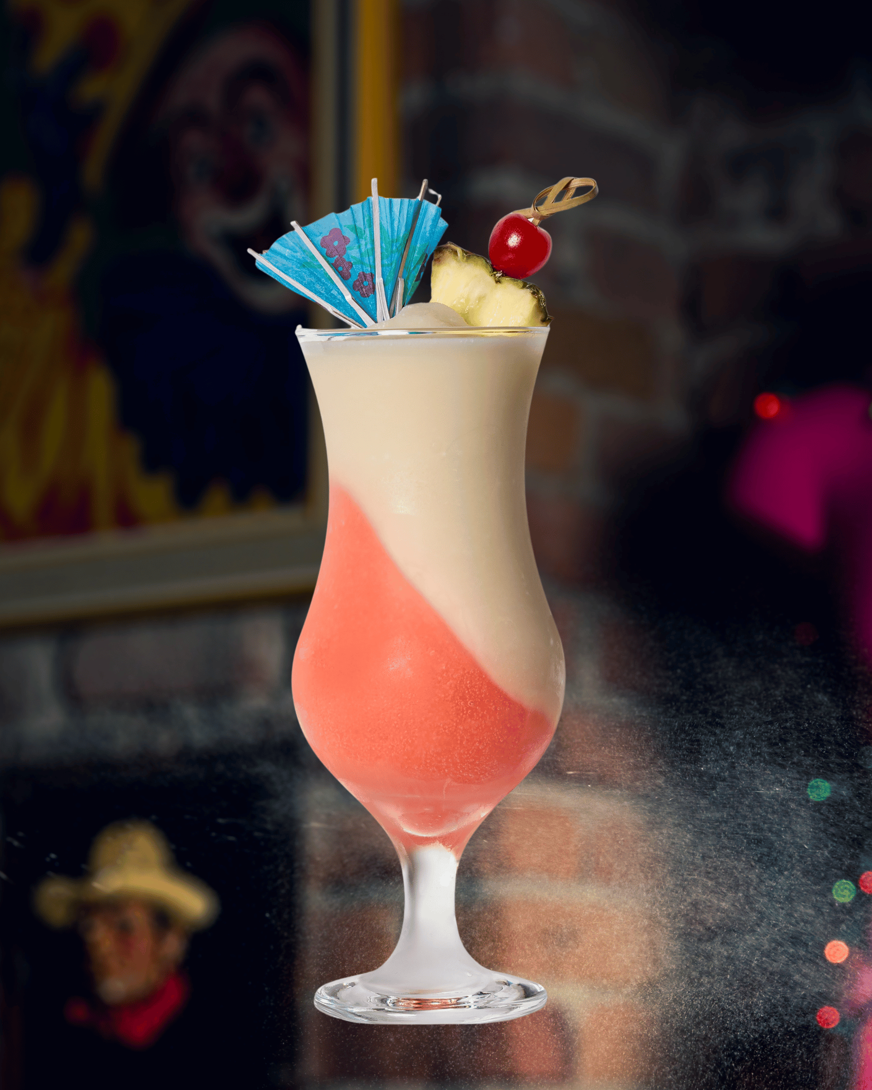 Cocktail coloré avec tranches d'ananas, cerise et un parasol, dans un verre tulipe