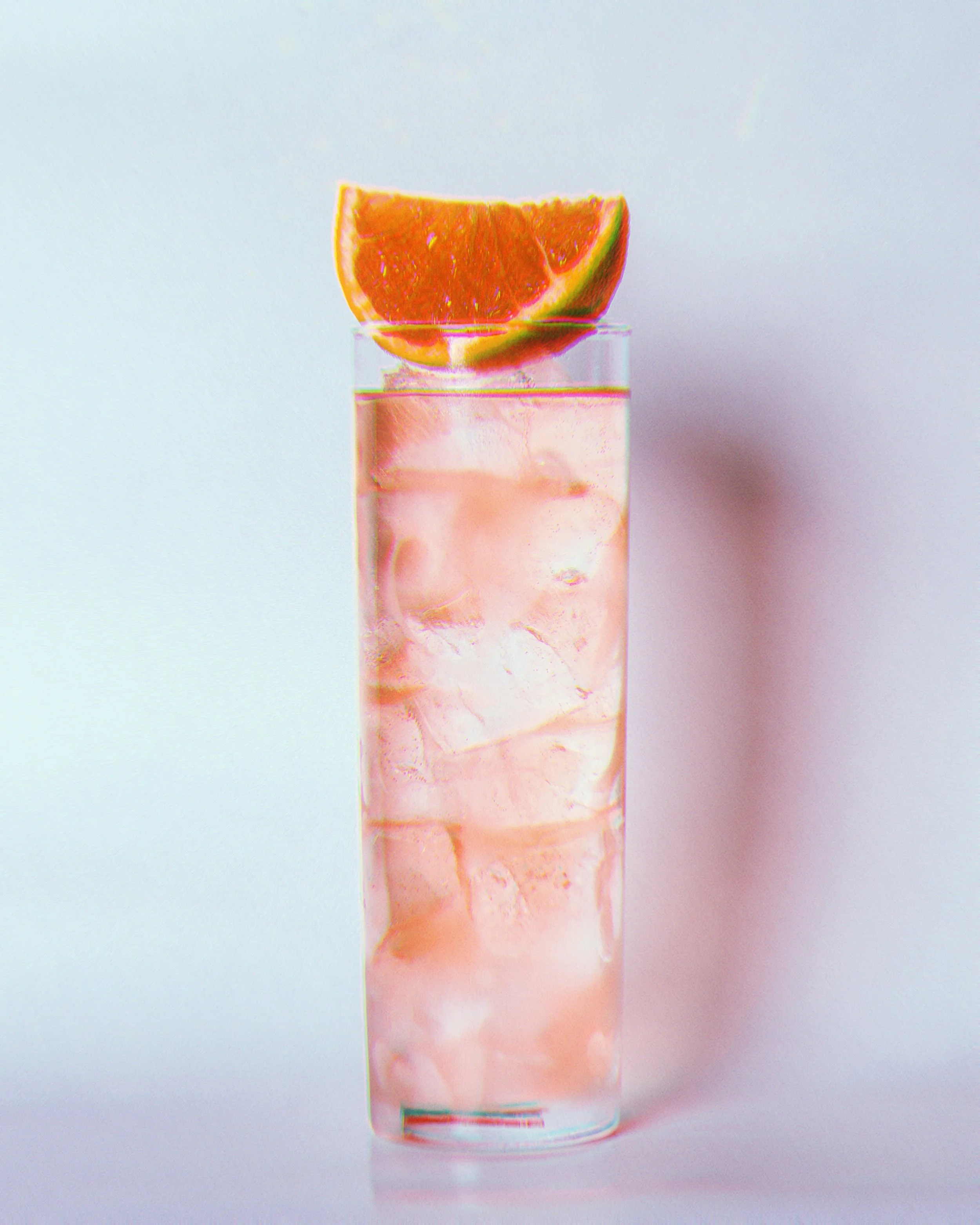 Verre transparent rempli de boisson rose avec glaçons et une tranche d'orange sur le bord