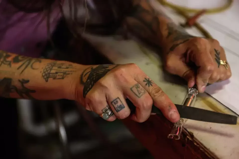 Tattooed hands holding a knife and cutting a piece of meat or food on a white surface.